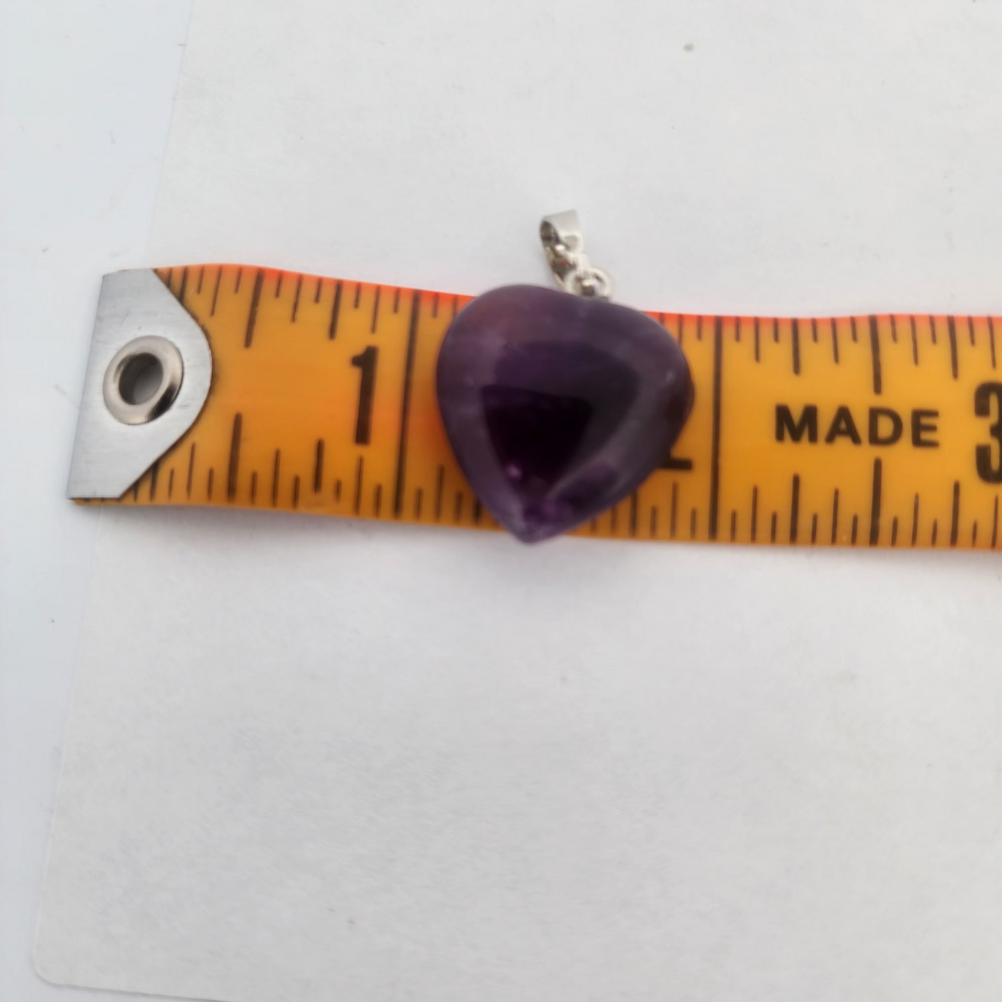 Purple heart-shaped pendant on a measuring tape against a white background