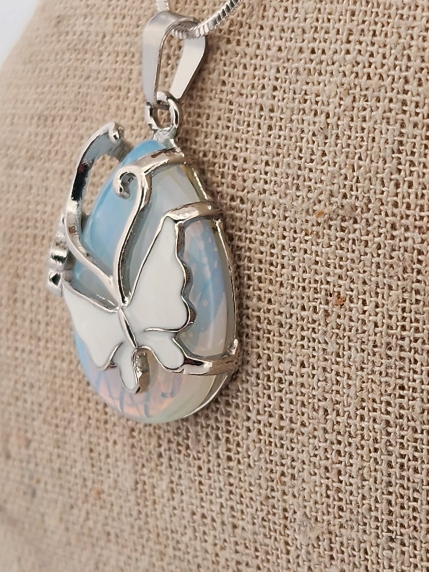 Butterfly-shaped pendant with opal-like center on beige fabric background