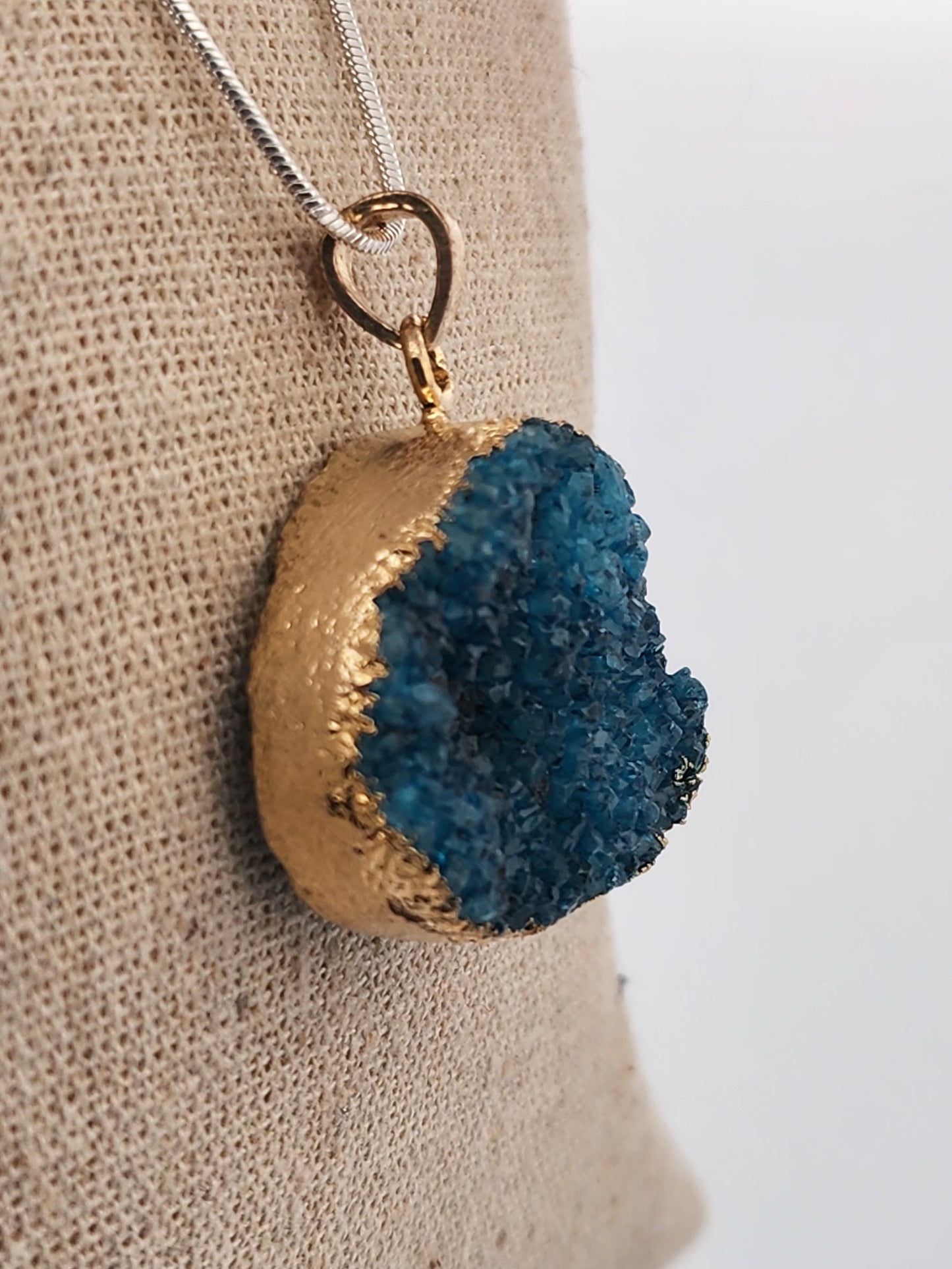 Necklace with a blue geode pendant on a beige surface