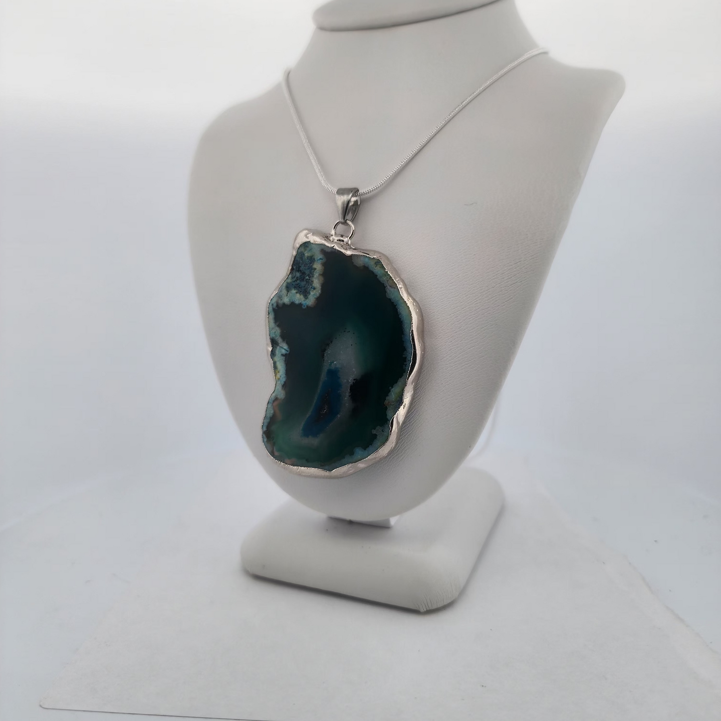 Necklace with a large green pendant on a mannequin bust against a white background
