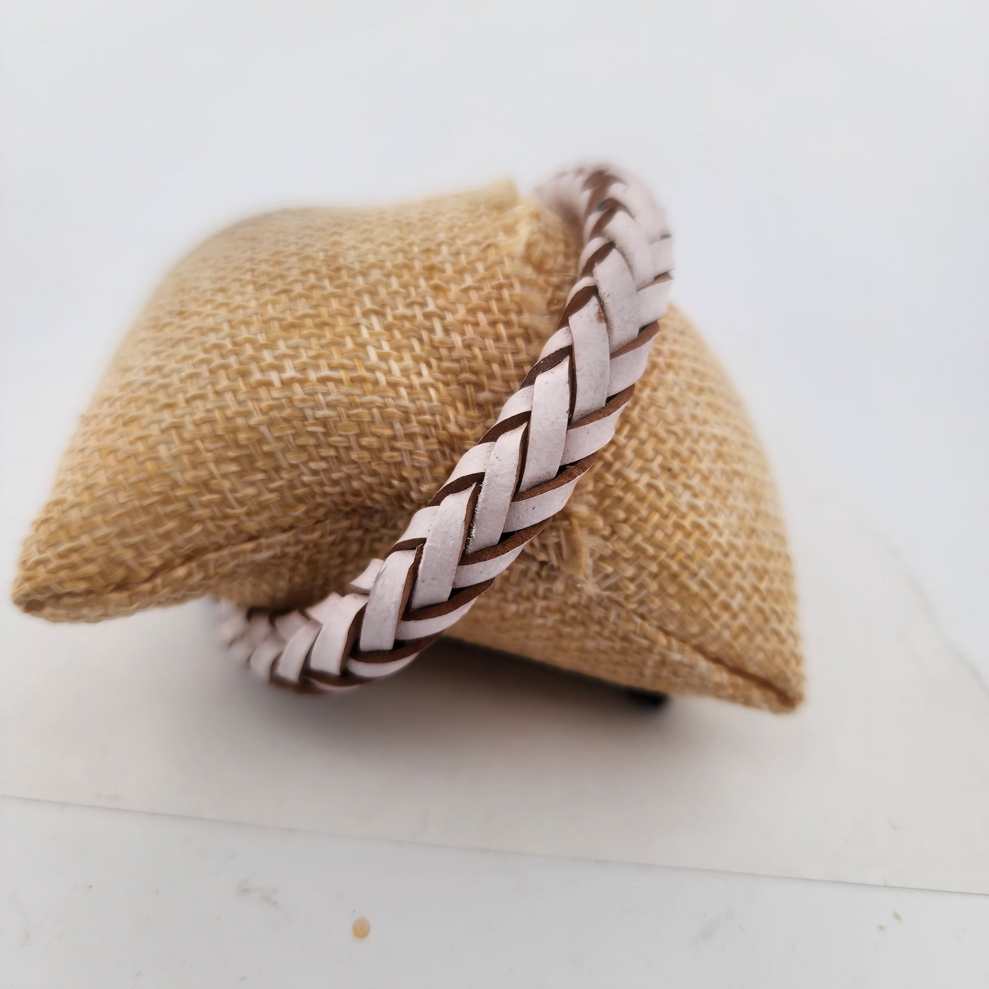 Braided leather bracelet on a textured beige pillow against a white background