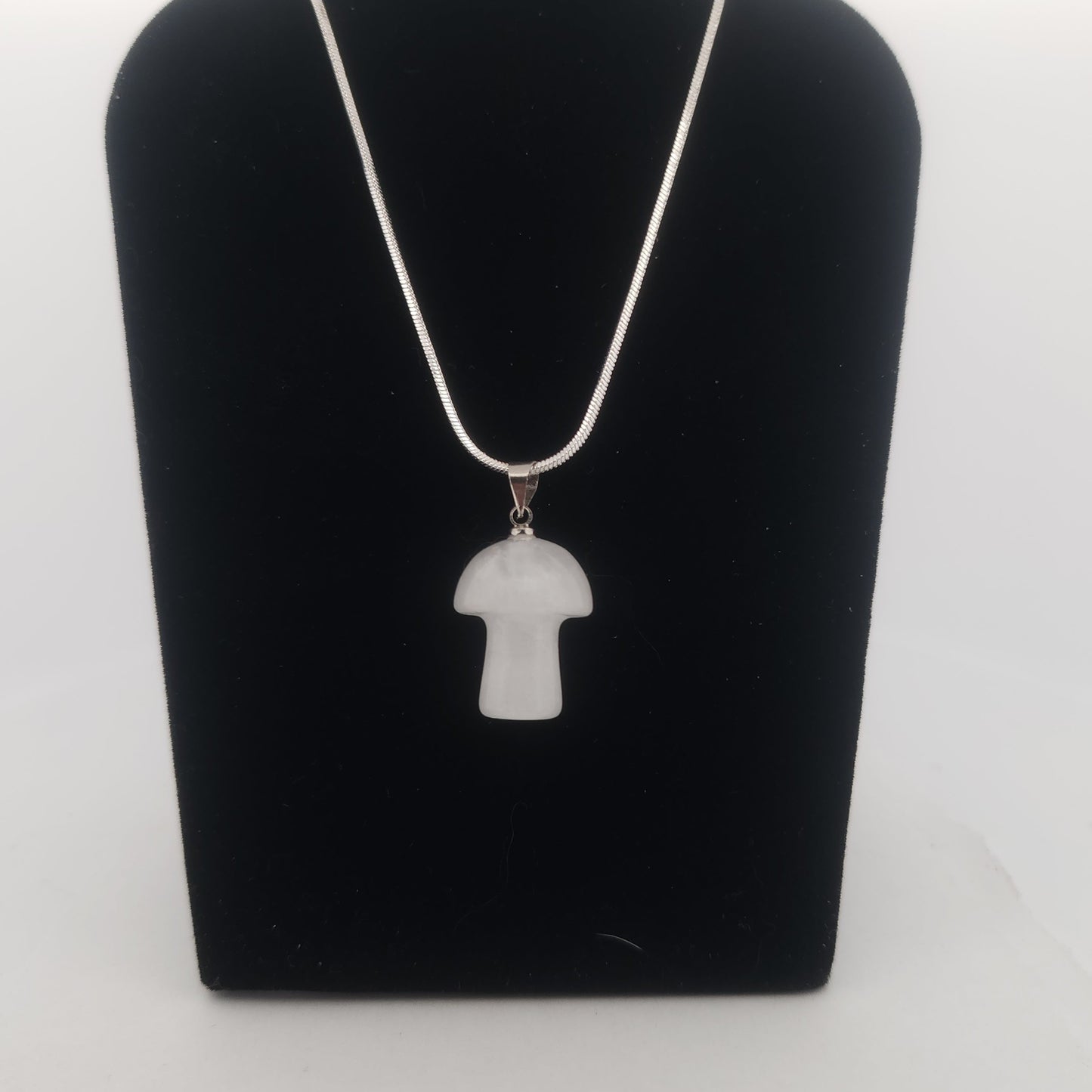 White pendant necklace on a black stand against a white background