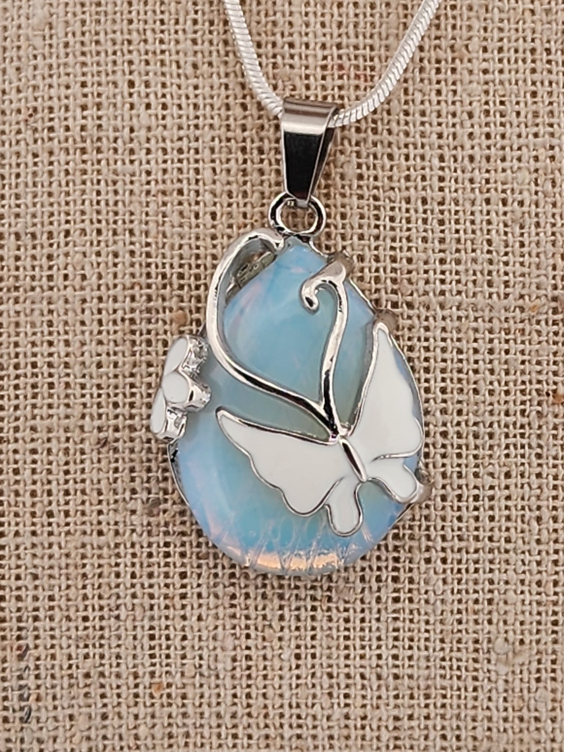 Butterfly-shaped pendant with blue and white design on a beige fabric background
