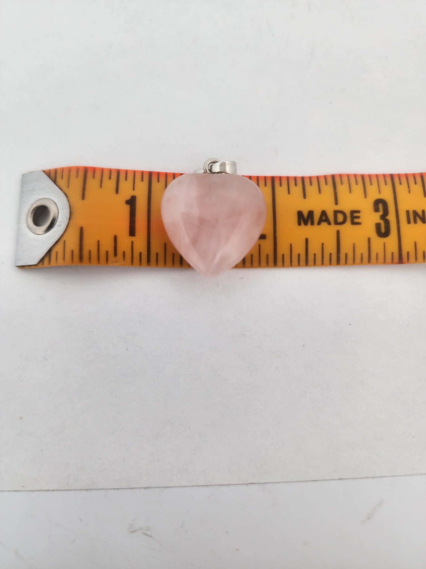 Heart-shaped rose quartz pendant on a measuring tape against a white background