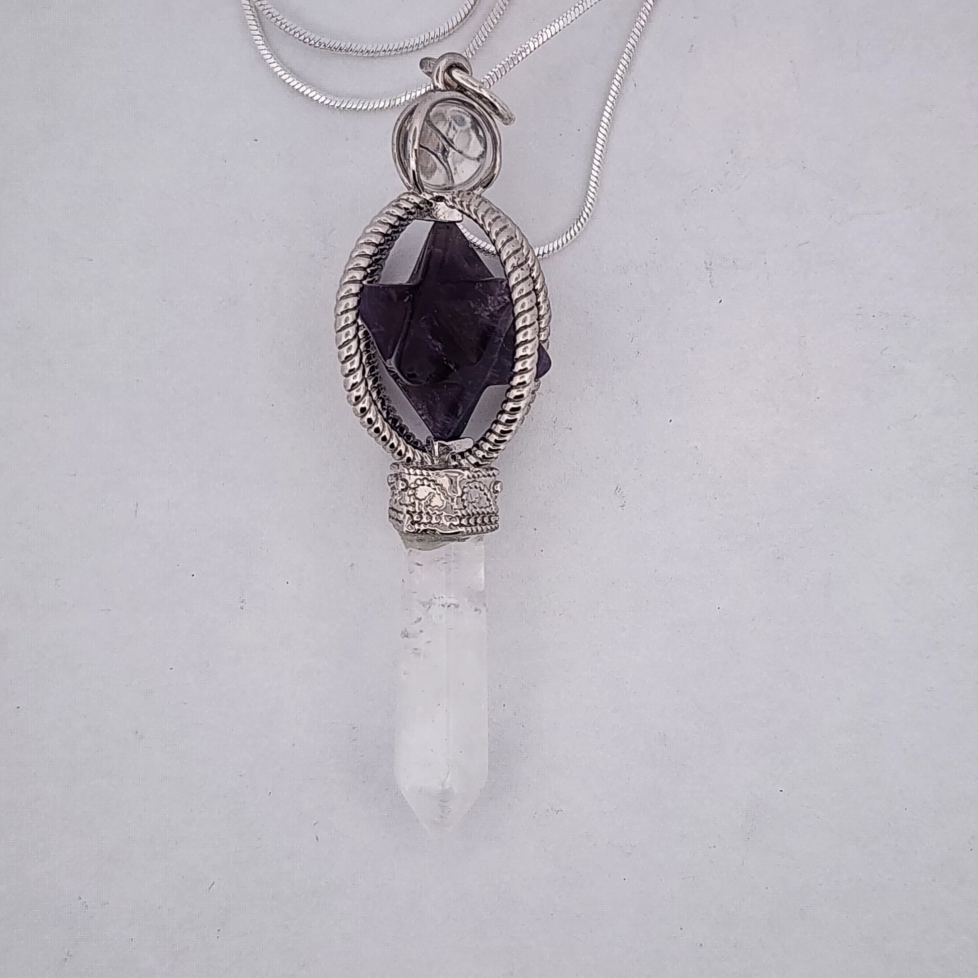 Necklace with a pendant featuring a dark purple gemstone and white crystal on a light gray background