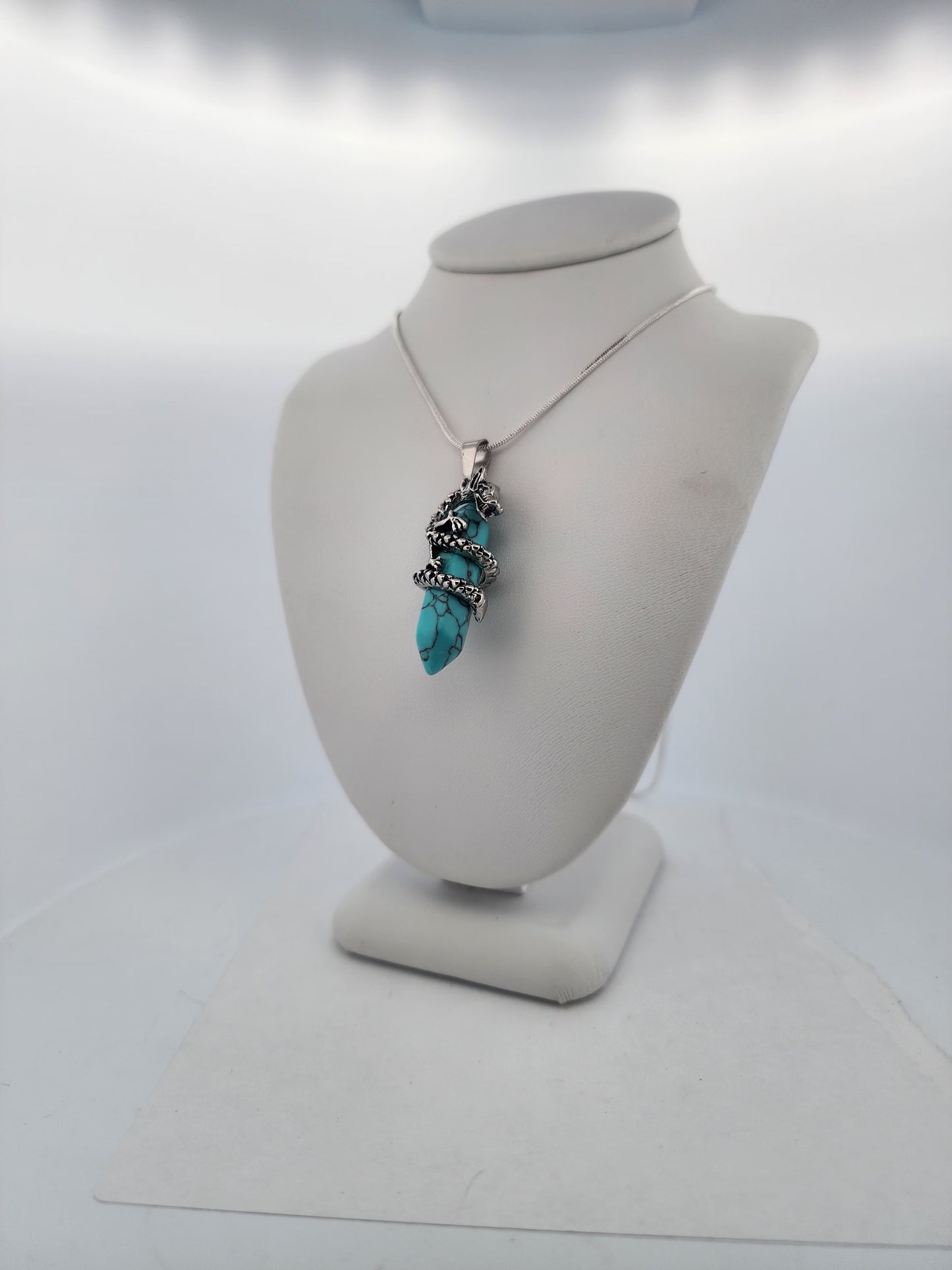 Necklace with a large turquoise pendant on a mannequin bust against a white background