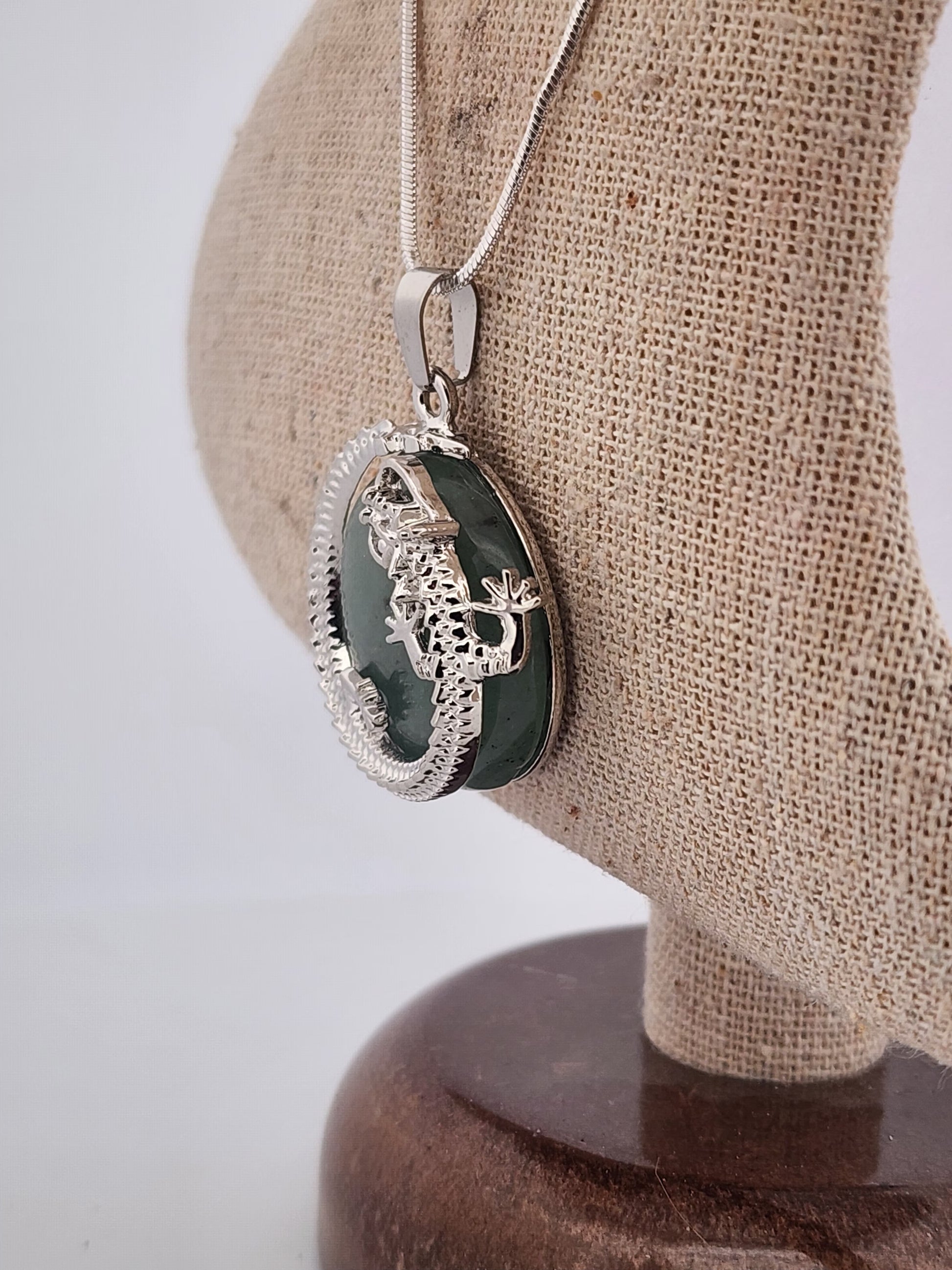 Silver pendant with green stone on a beige stand against a white background
