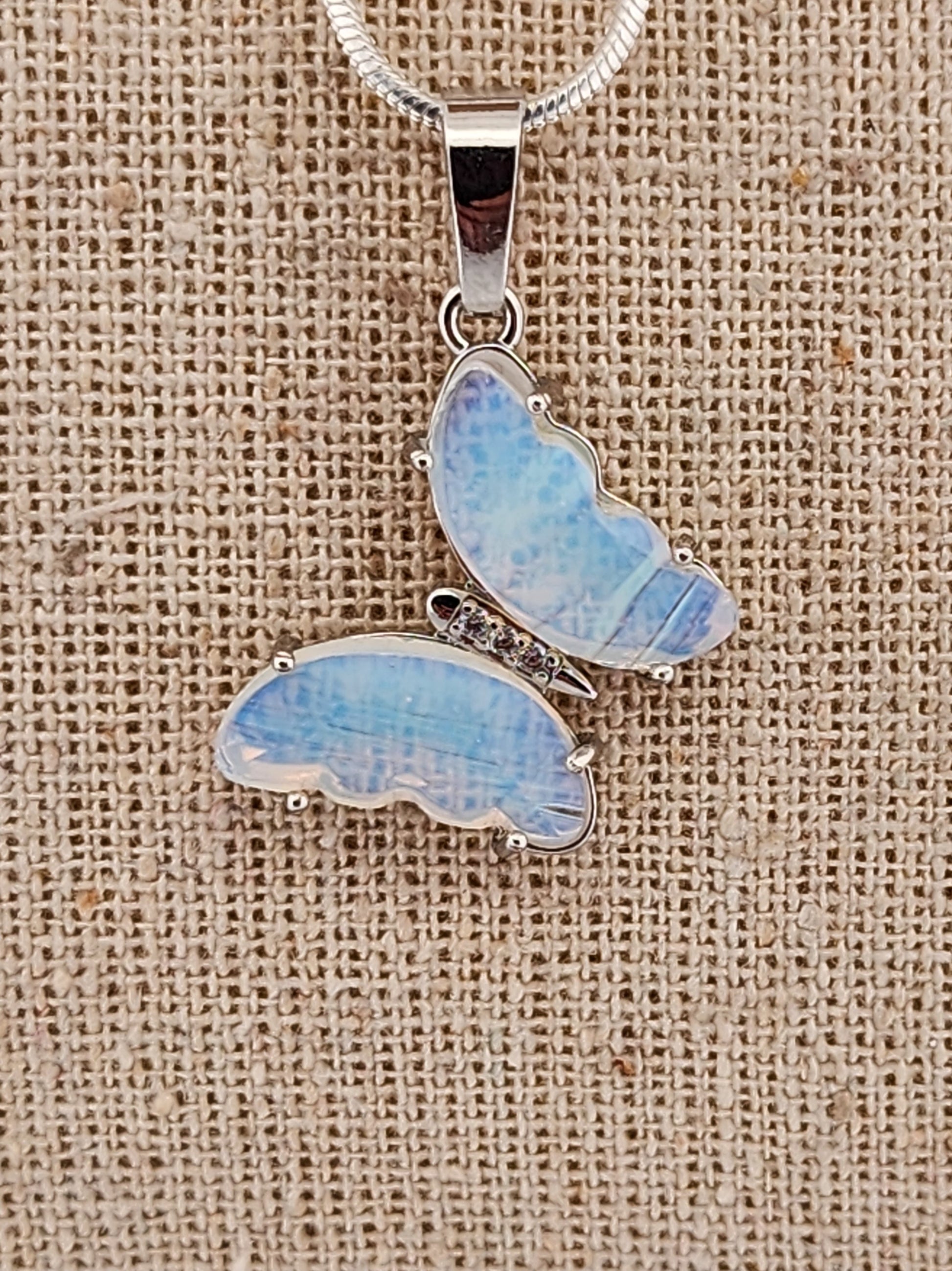 Butterfly-shaped pendant with blue and white pattern on a beige fabric background