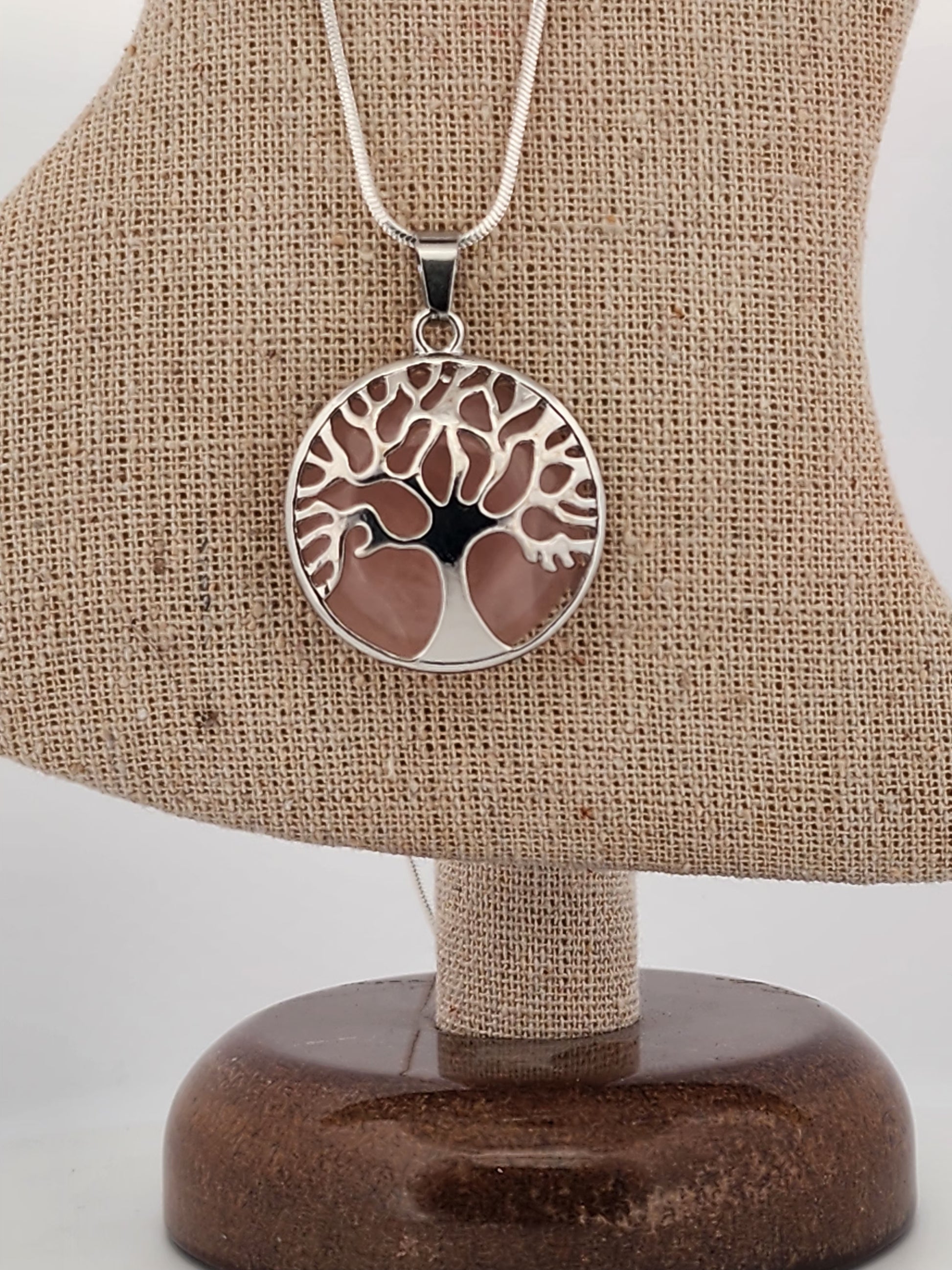 Silver necklace with a tree of life pendant on a brown fabric stand.