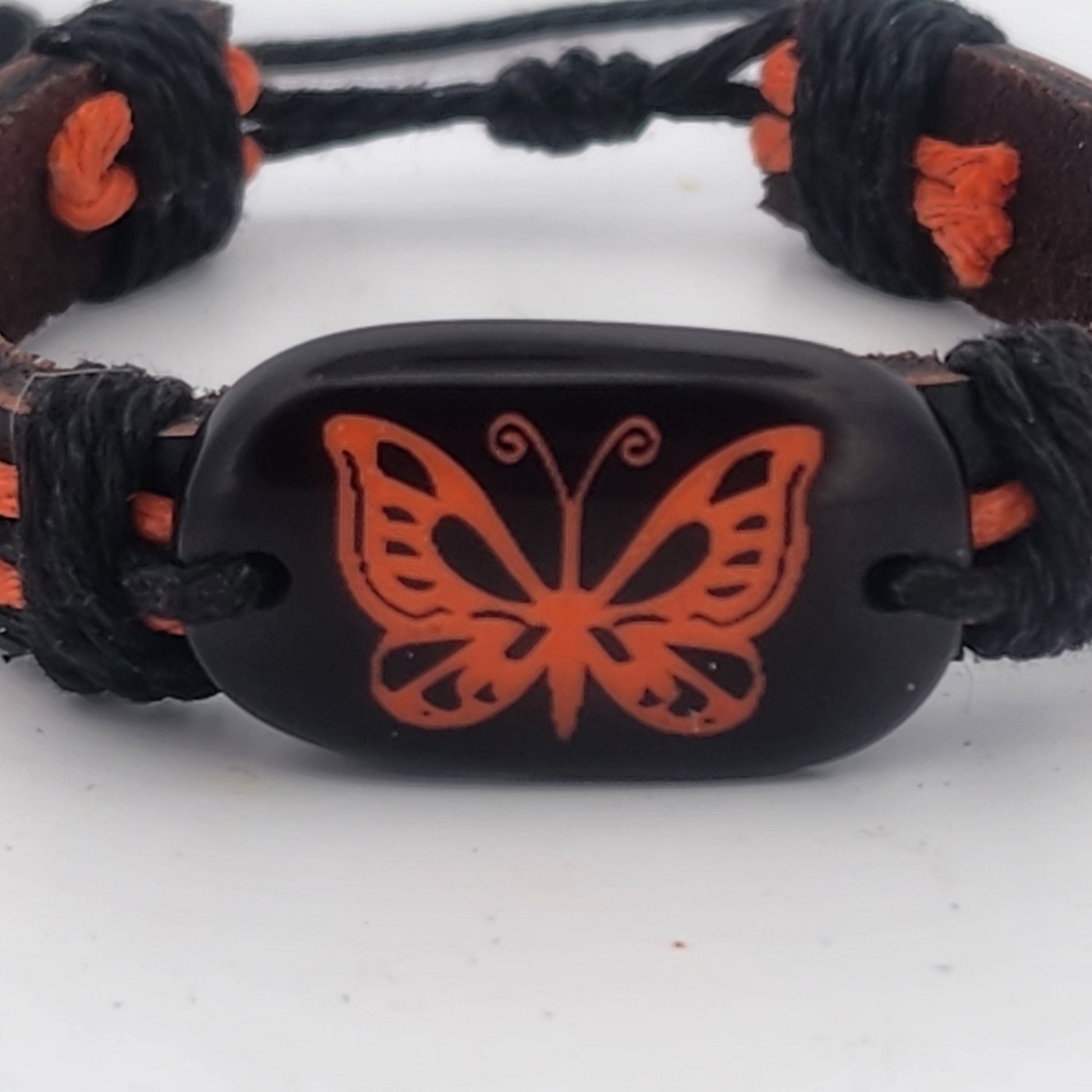 Bracelet with orange butterfly design on a black cord against a white background