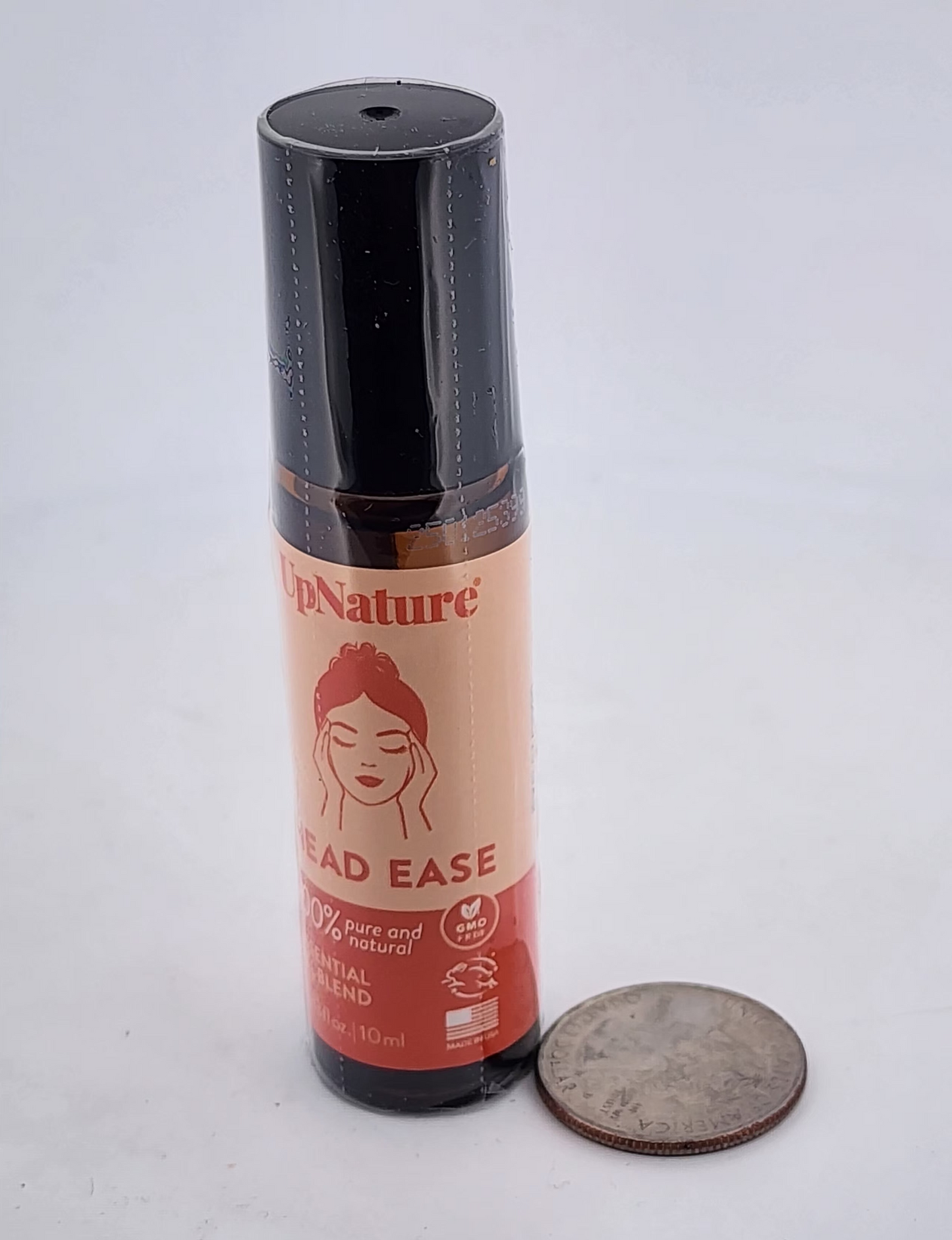 Small bottle labeled 'Head Ease' by 'In Nature' on a white background with a quarter for scale.