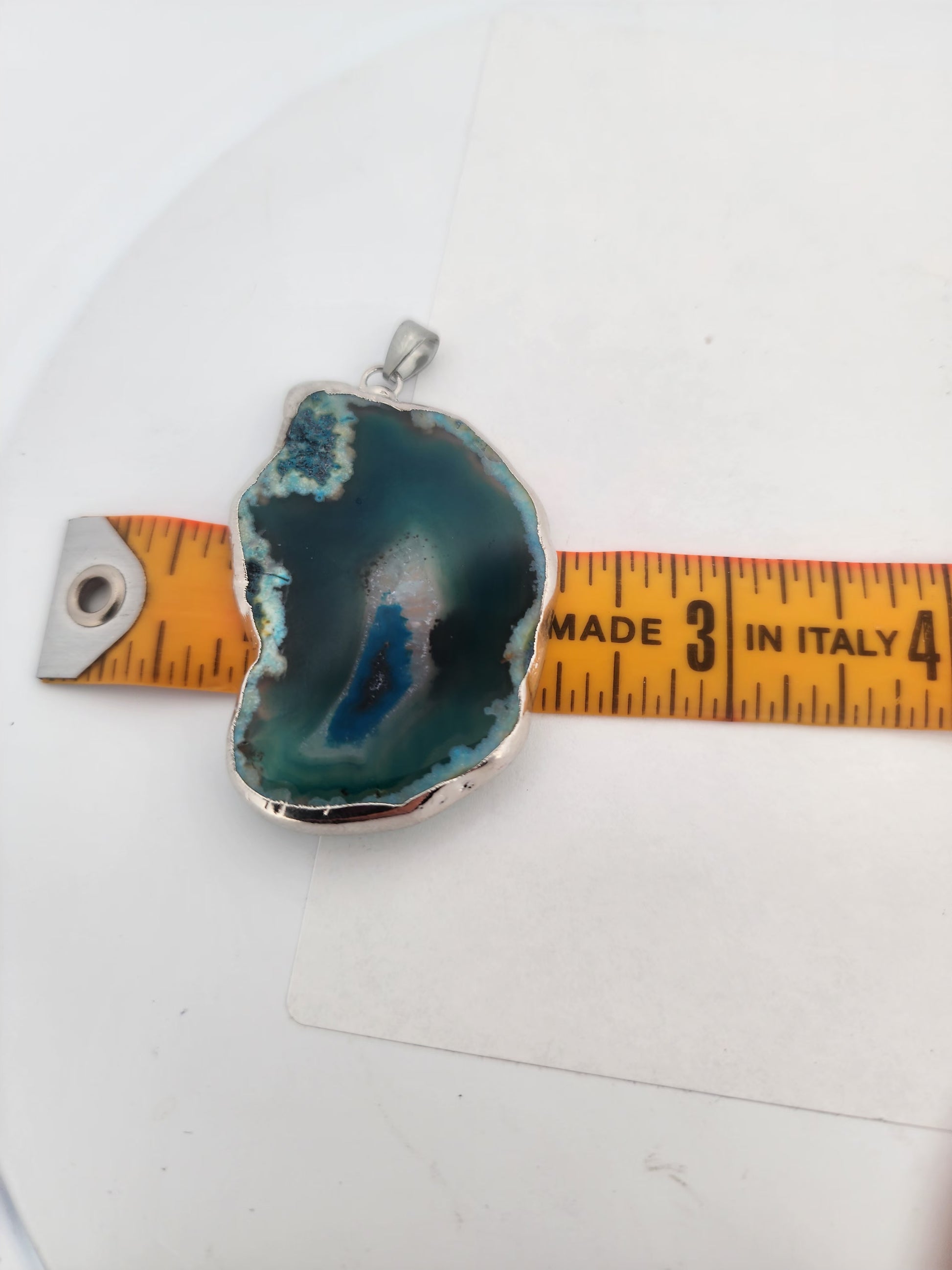 Agate pendant with silver setting on a white background, measured by a yellow ruler.