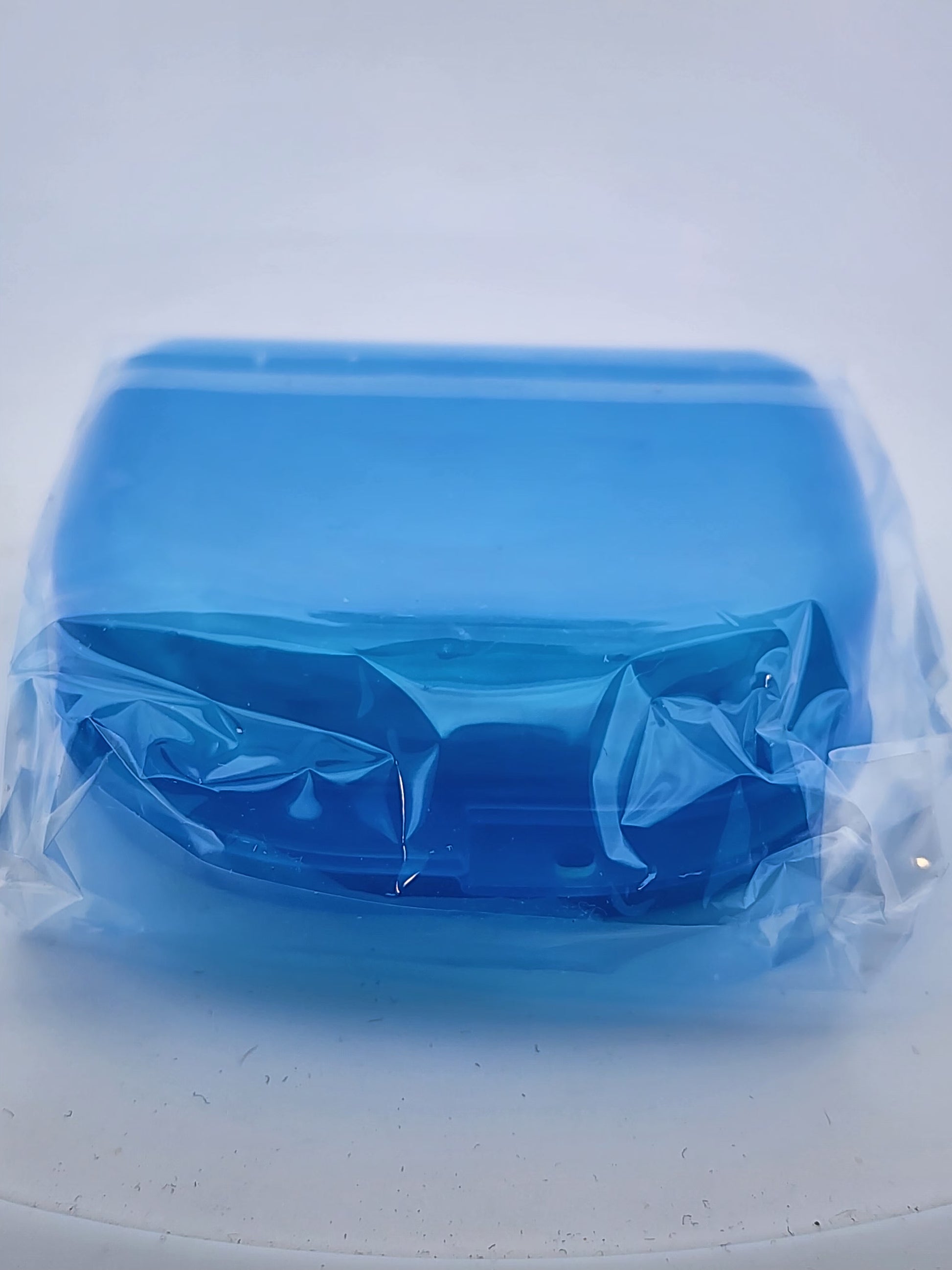 Blue plastic container with a lid in clear plastic wrap on a white surface