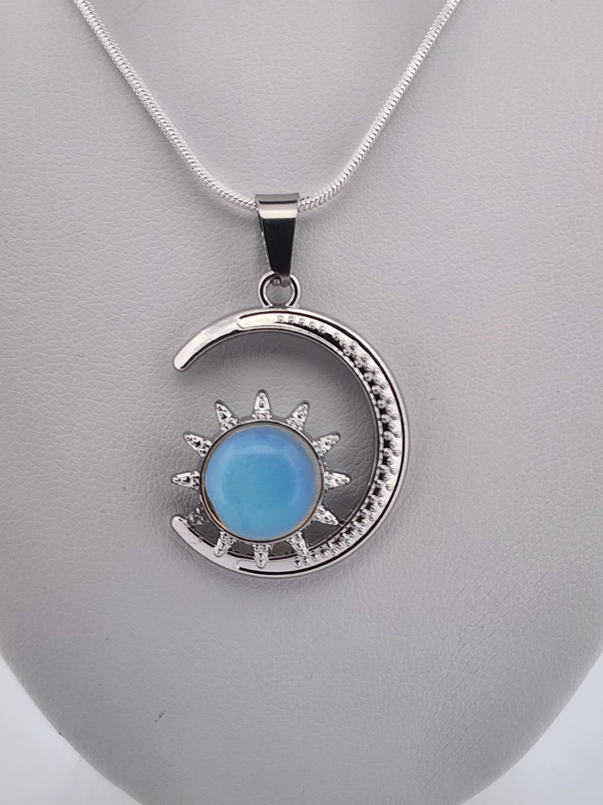Silver pendant with a blue gemstone on a gray stand