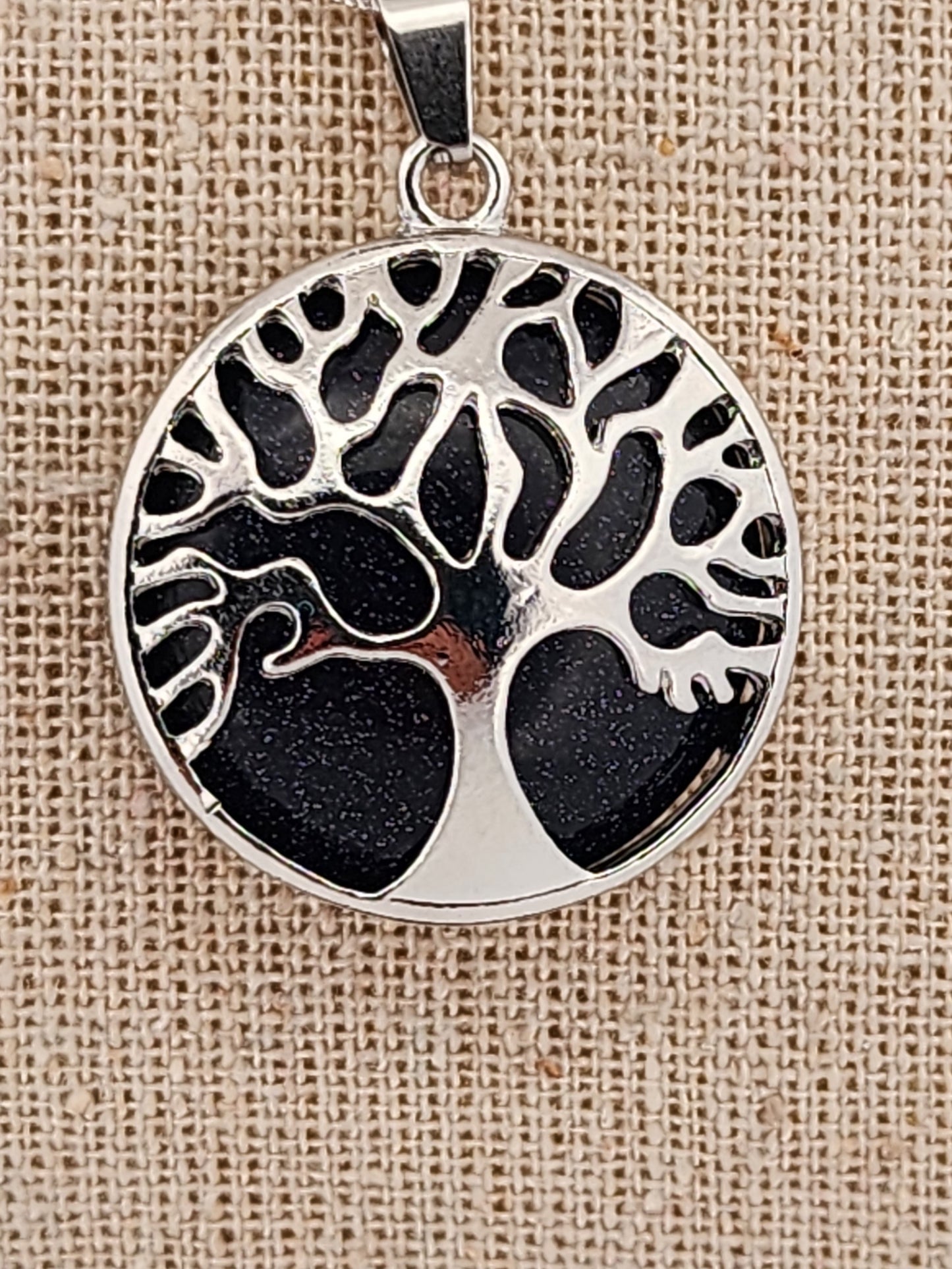 Silver pendant with tree design on a textured beige background