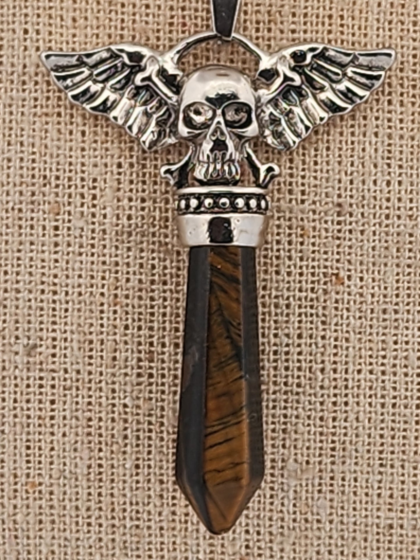 Pendant with skull design and wings on a wooden handle against a beige background
