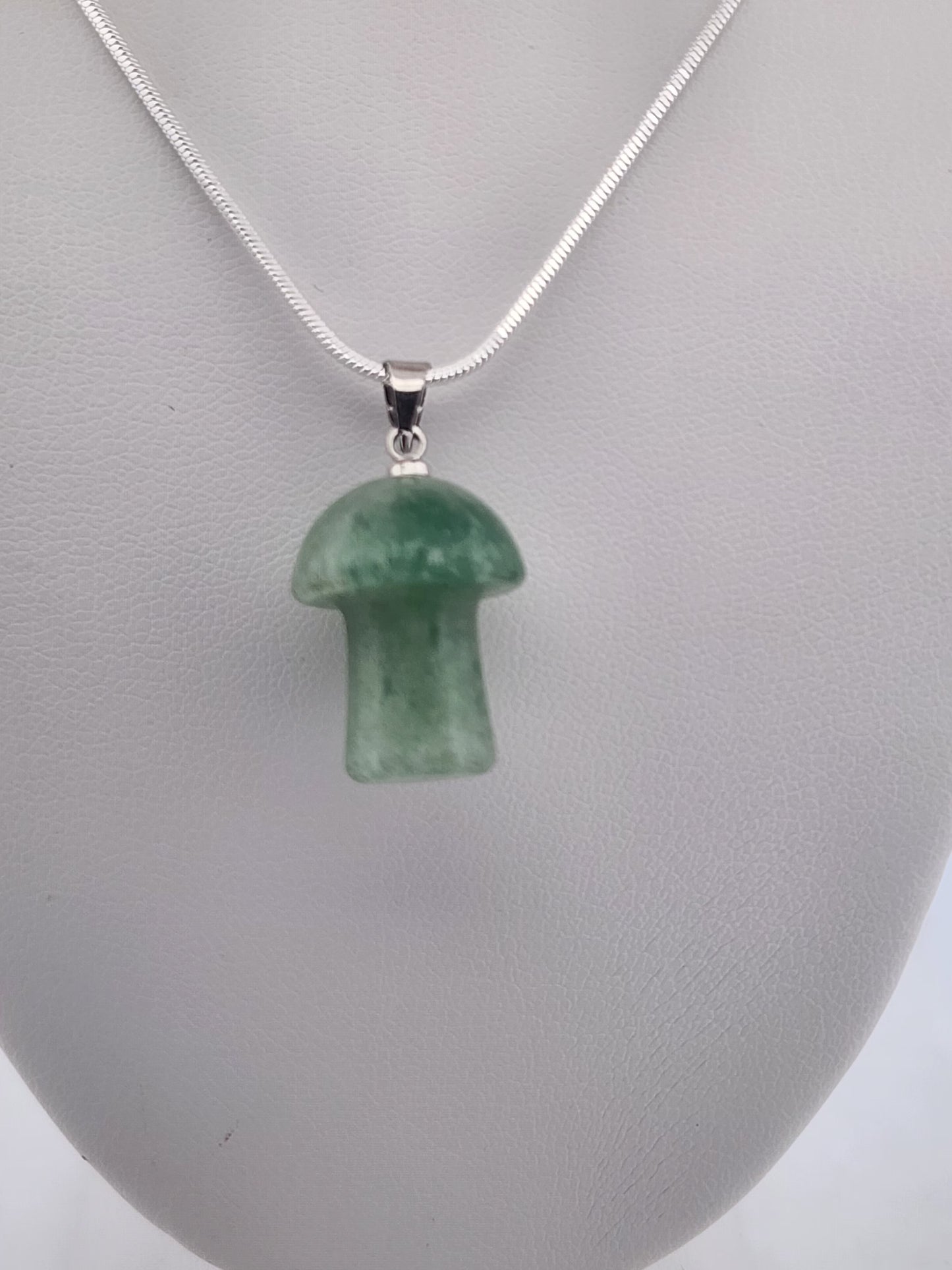 Green mushroom-shaped pendant on a silver chain against a gray background