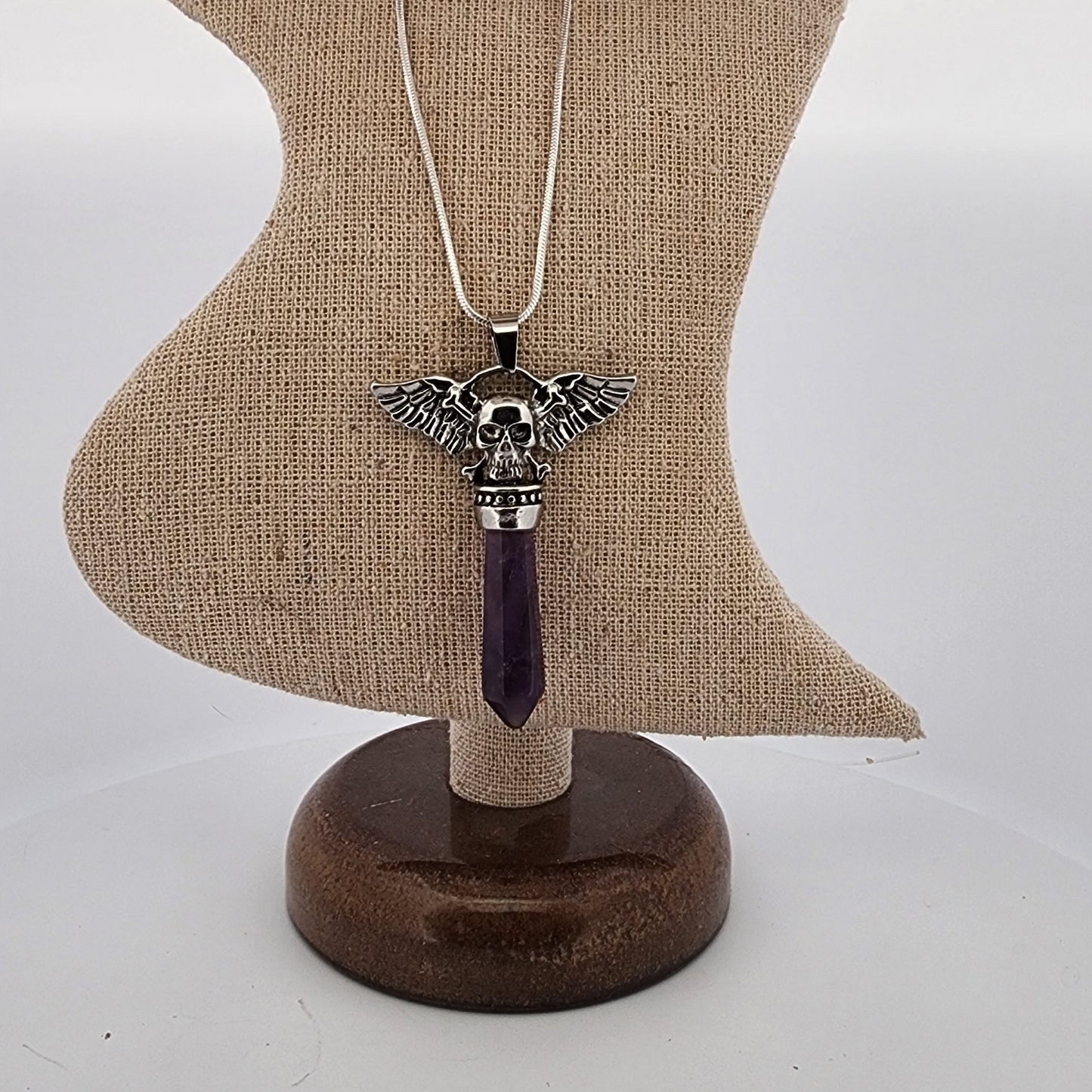 Necklace with a skull and wings pendant on a wooden stand against a white background