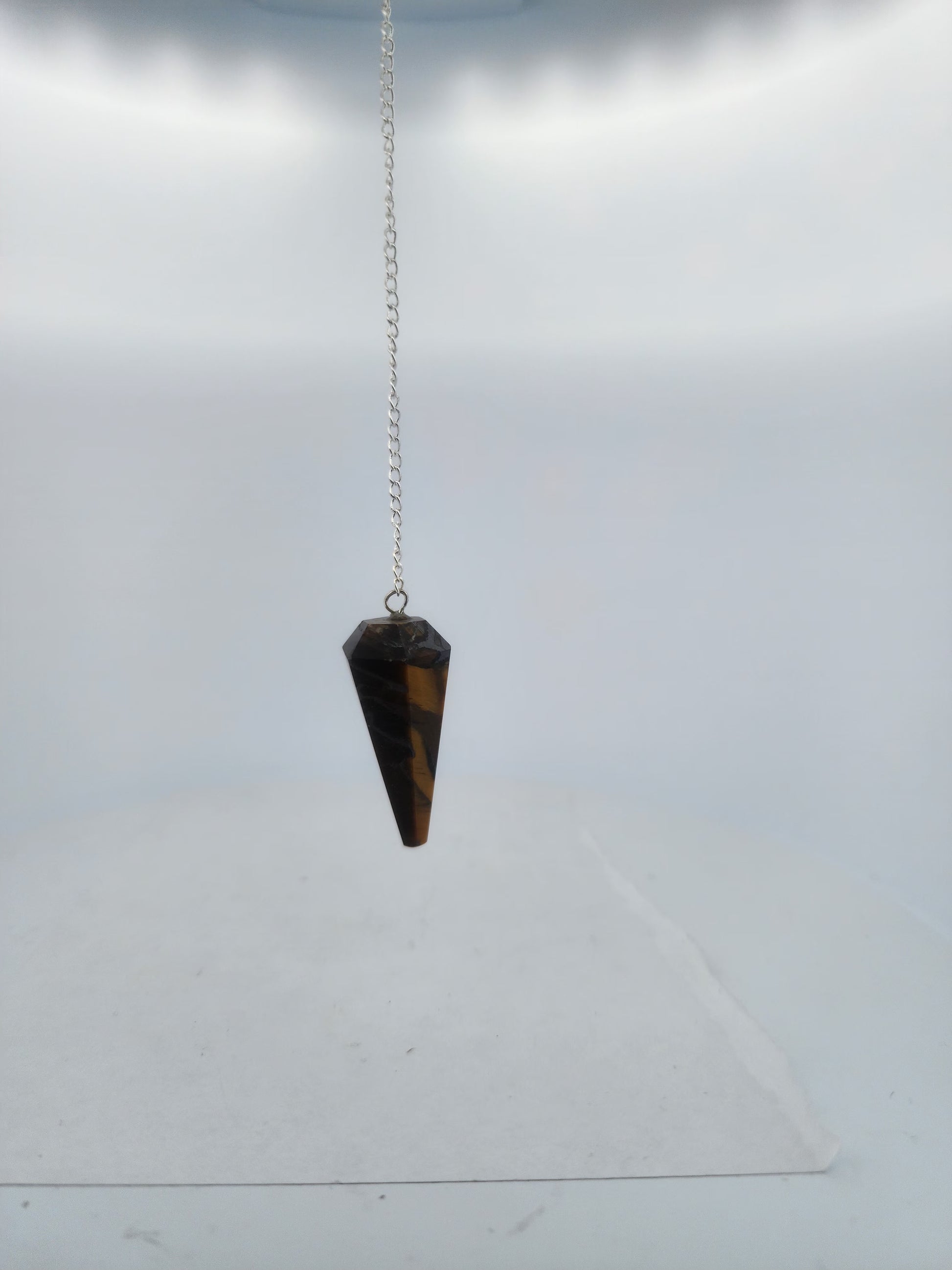 Tiger eye pendulum on a chain against a white background