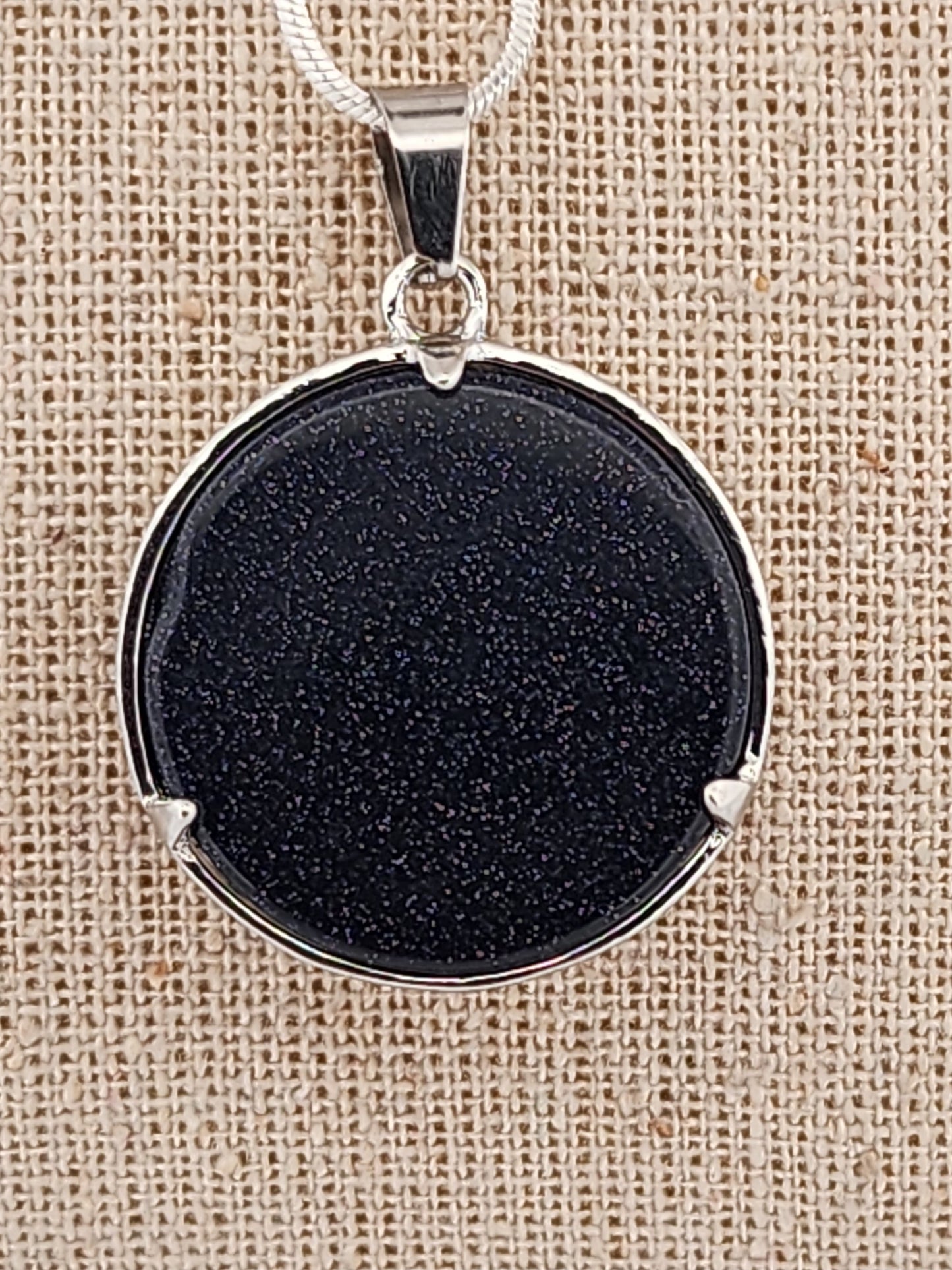 Black stone pendant with silver frame on a beige fabric background