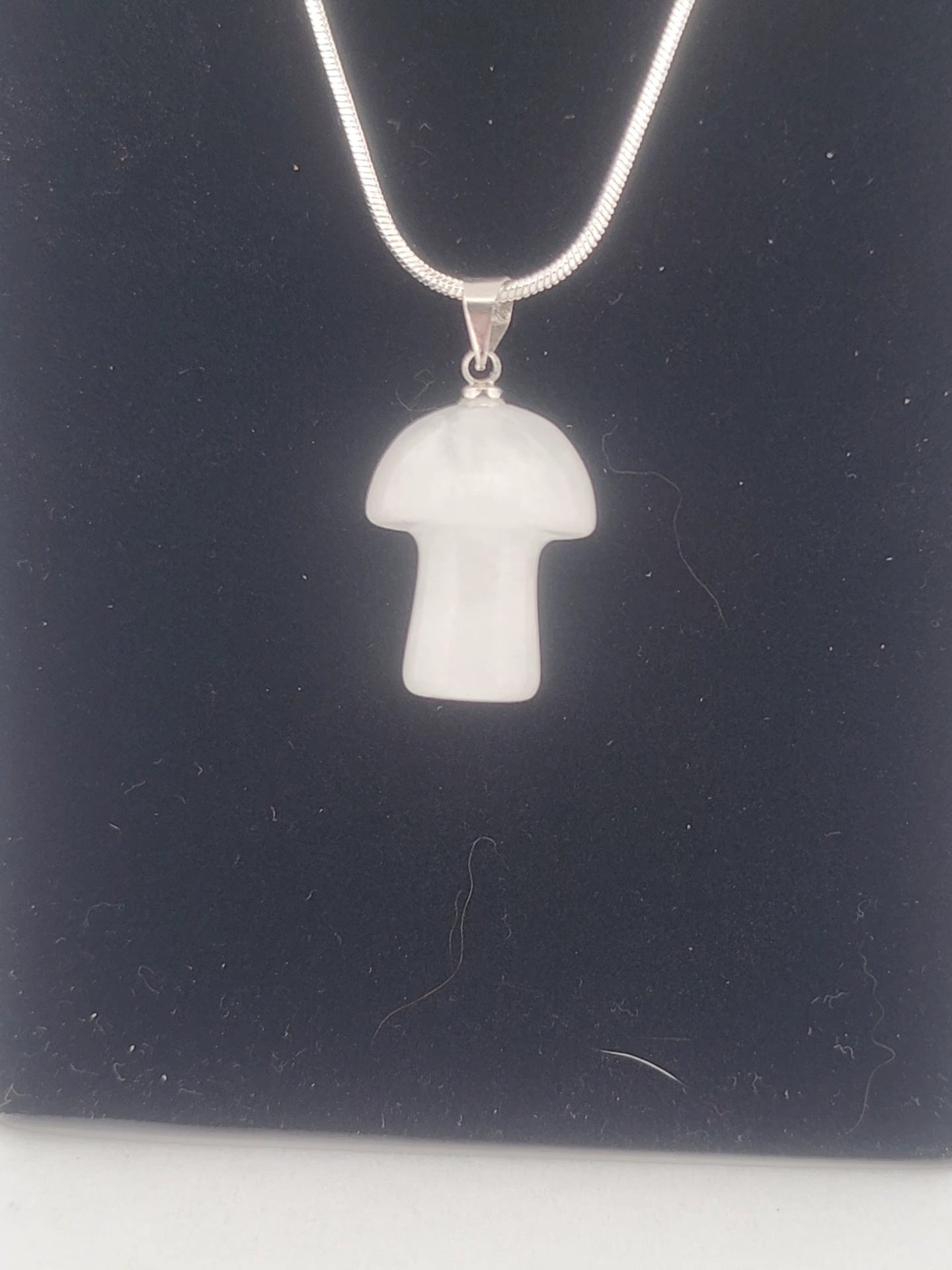 Mushroom-shaped pendant on a chain against a dark background