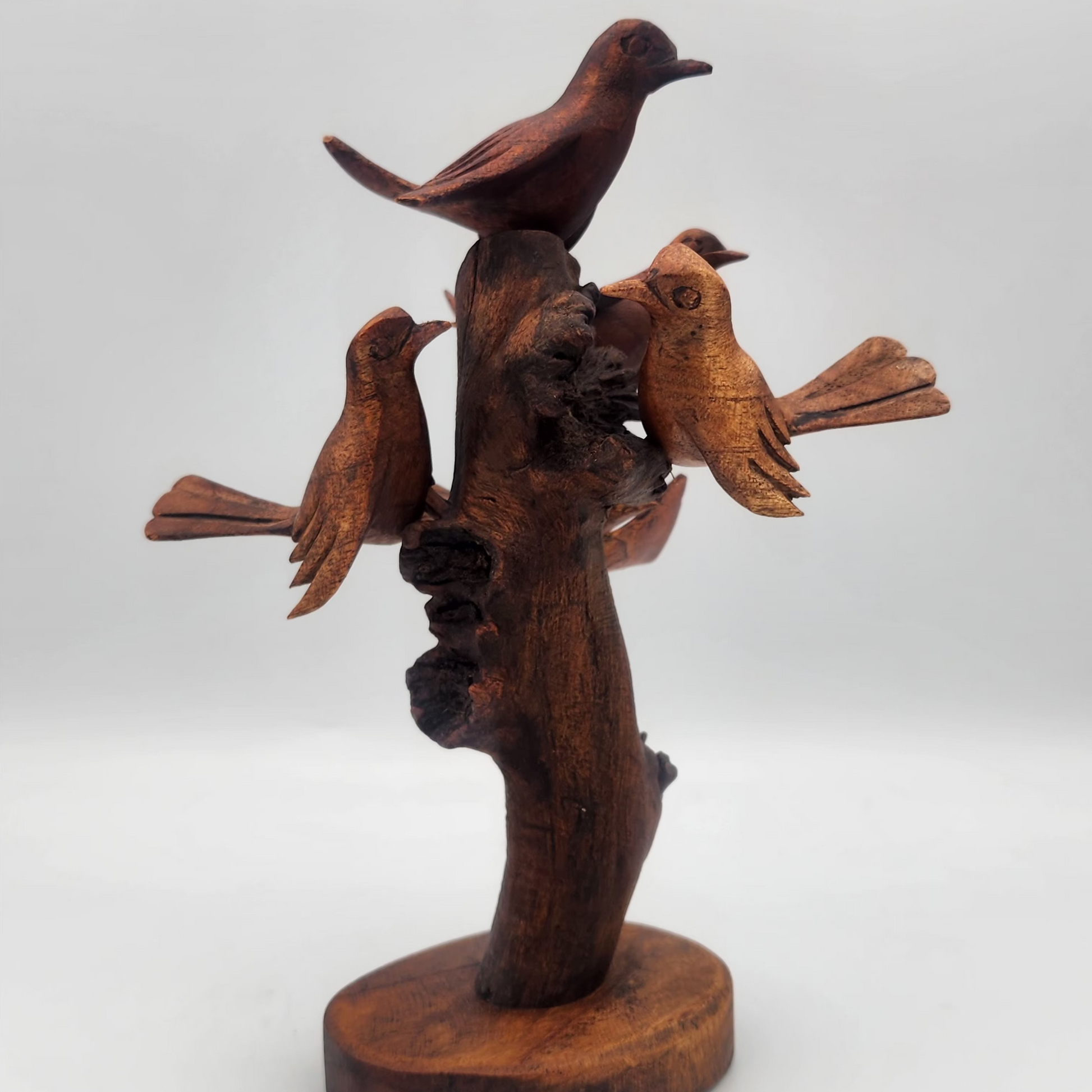 Wooden sculpture of three birds perched on a branch on a white background