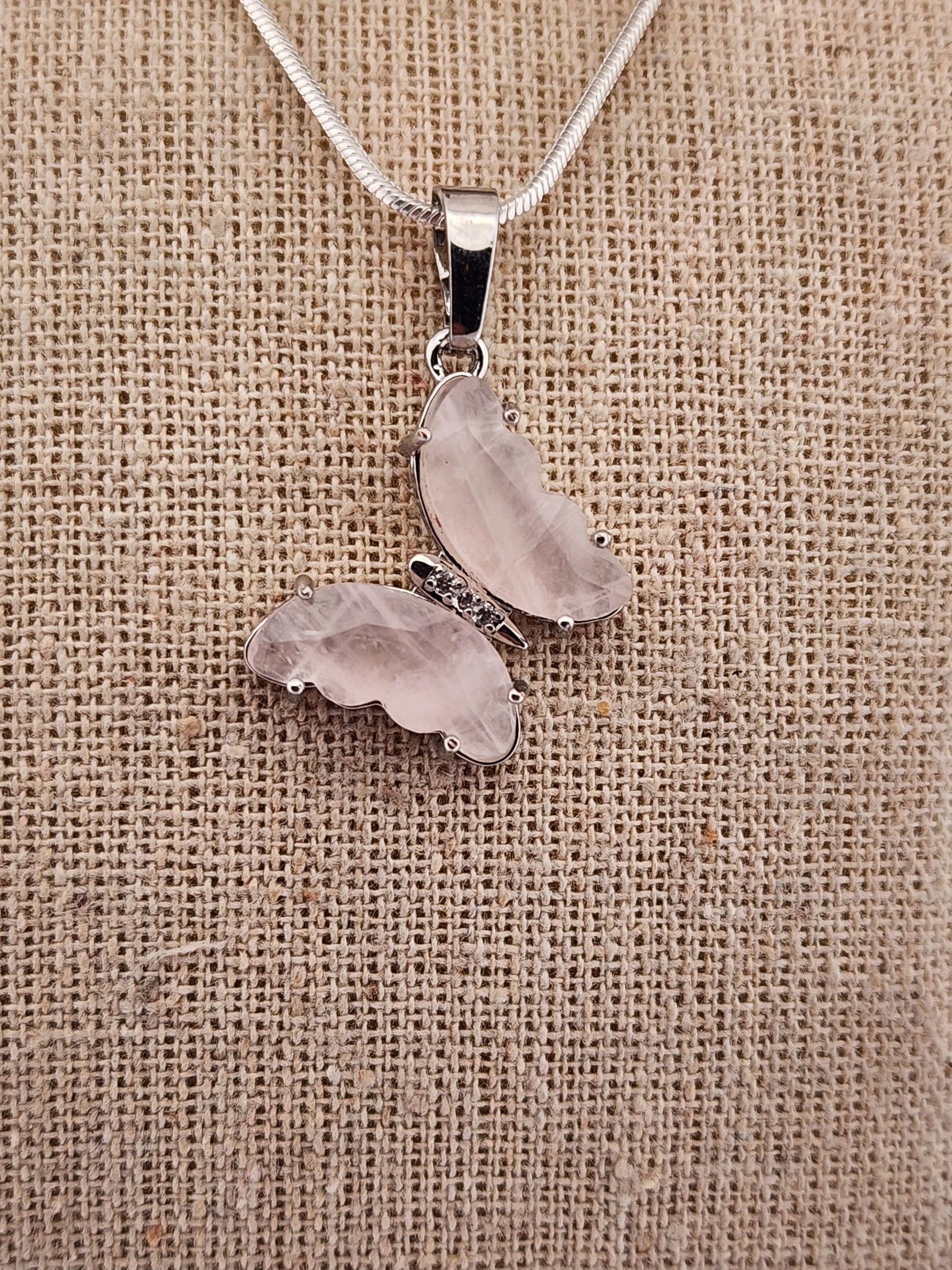 Silver necklace with two heart-shaped pendants on a textured beige background