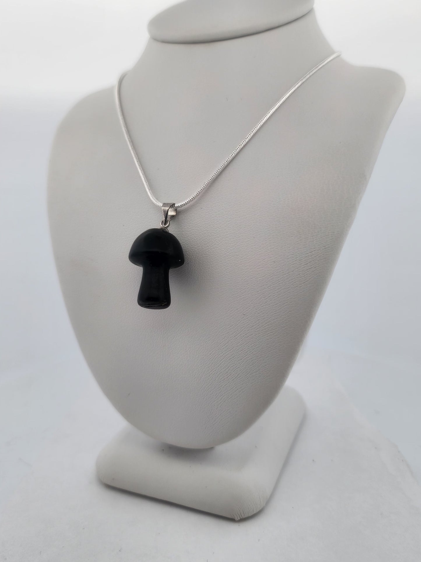 Black mushroom pendant on a silver chain displayed on a gray bust