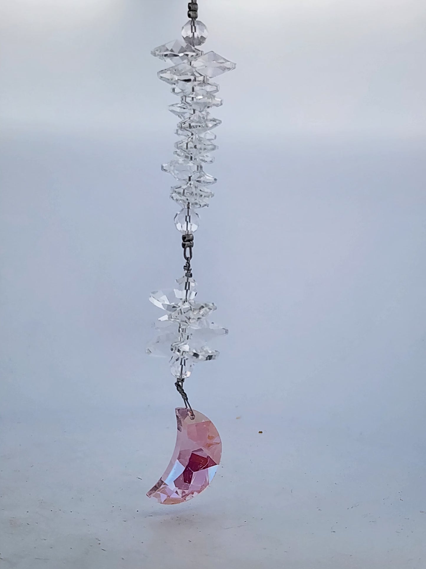 Crystal hanging ornament with a pink crescent moon charm on a light gray background