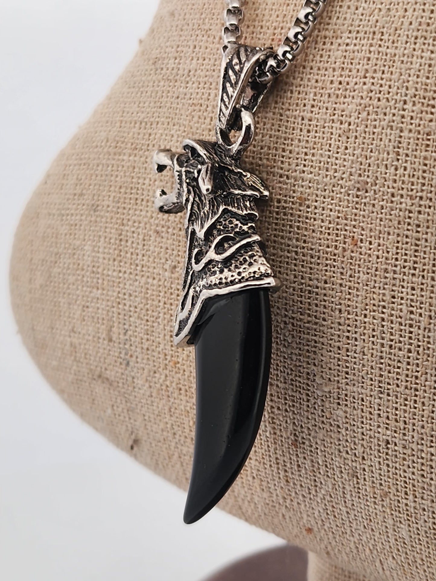 Necklace with a black pendant and silver horse head design on a beige fabric background