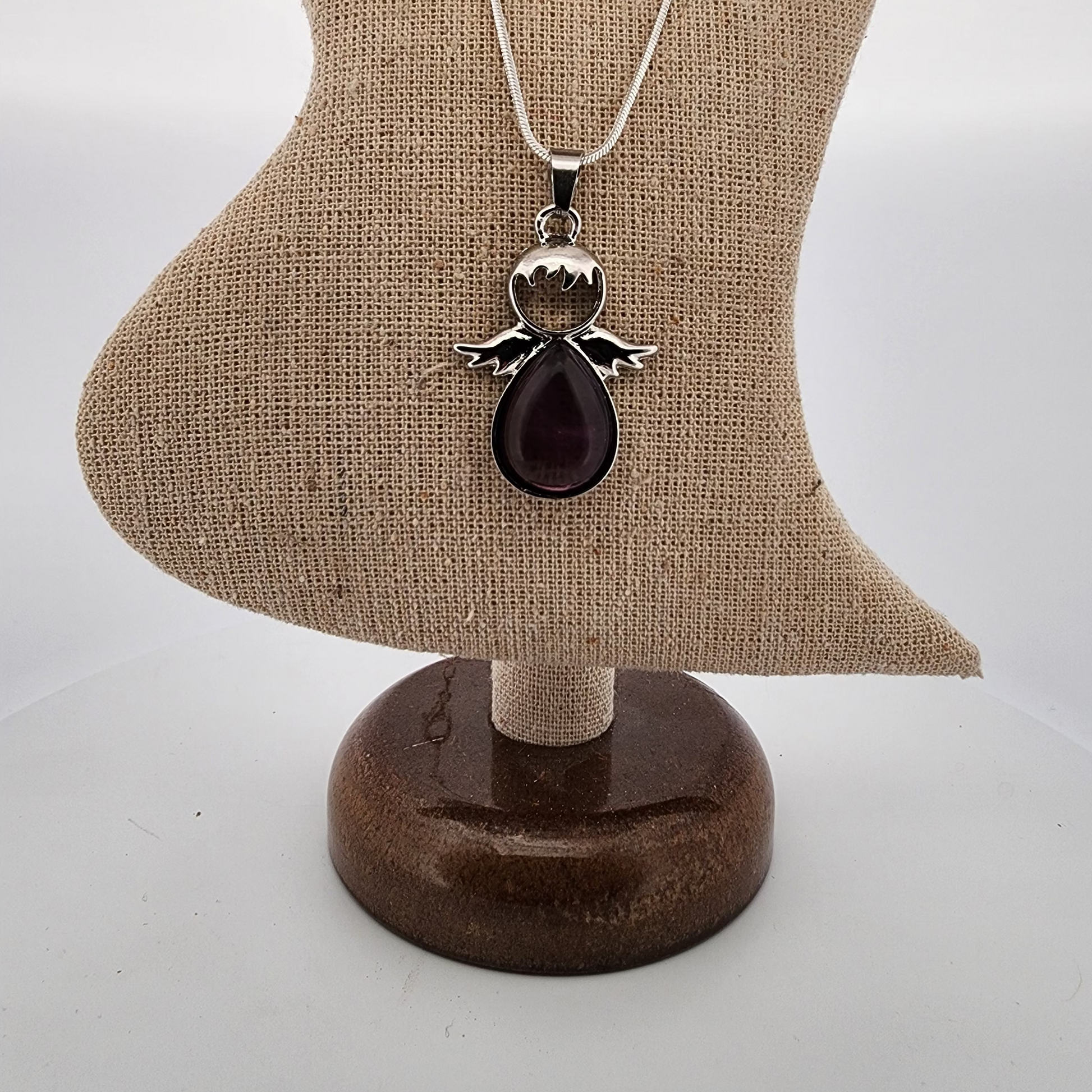 Necklace with an angel pendant and red stone on a brown stand against a white background