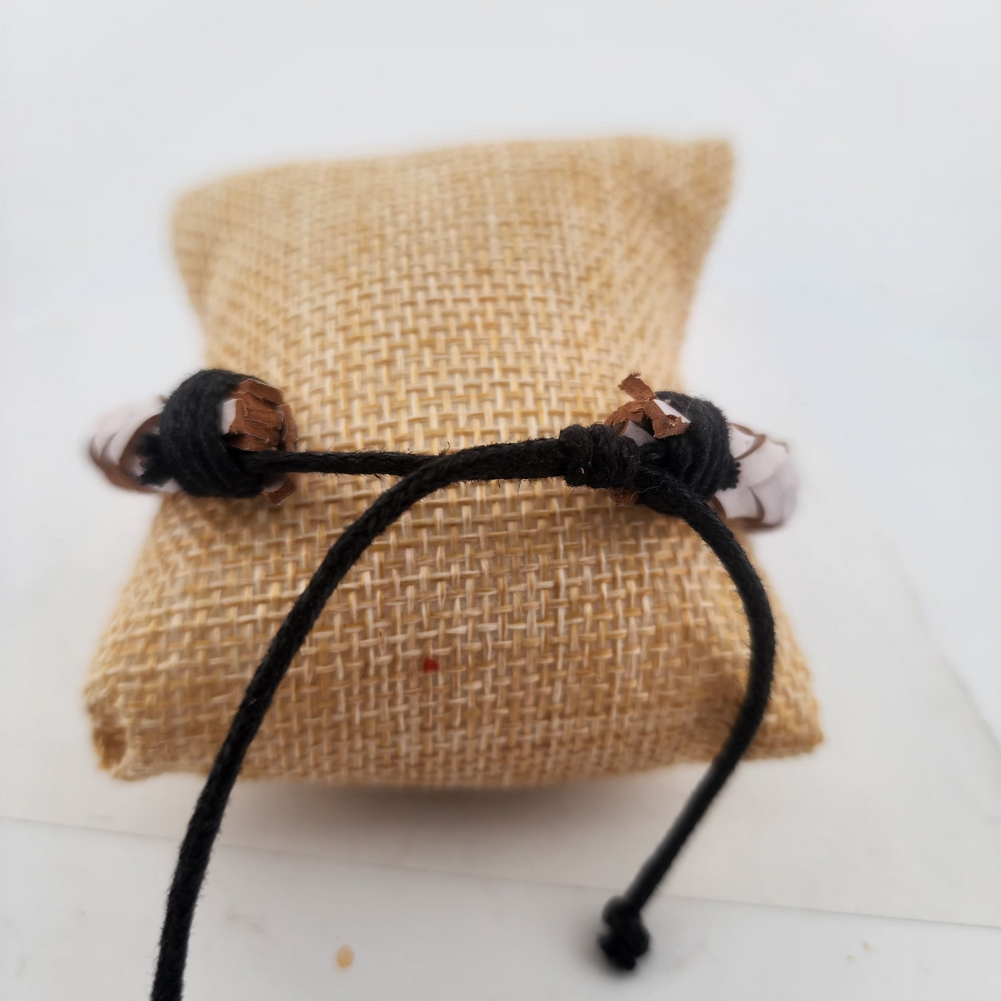 Black braided bracelet on a burlap pillow with a white background