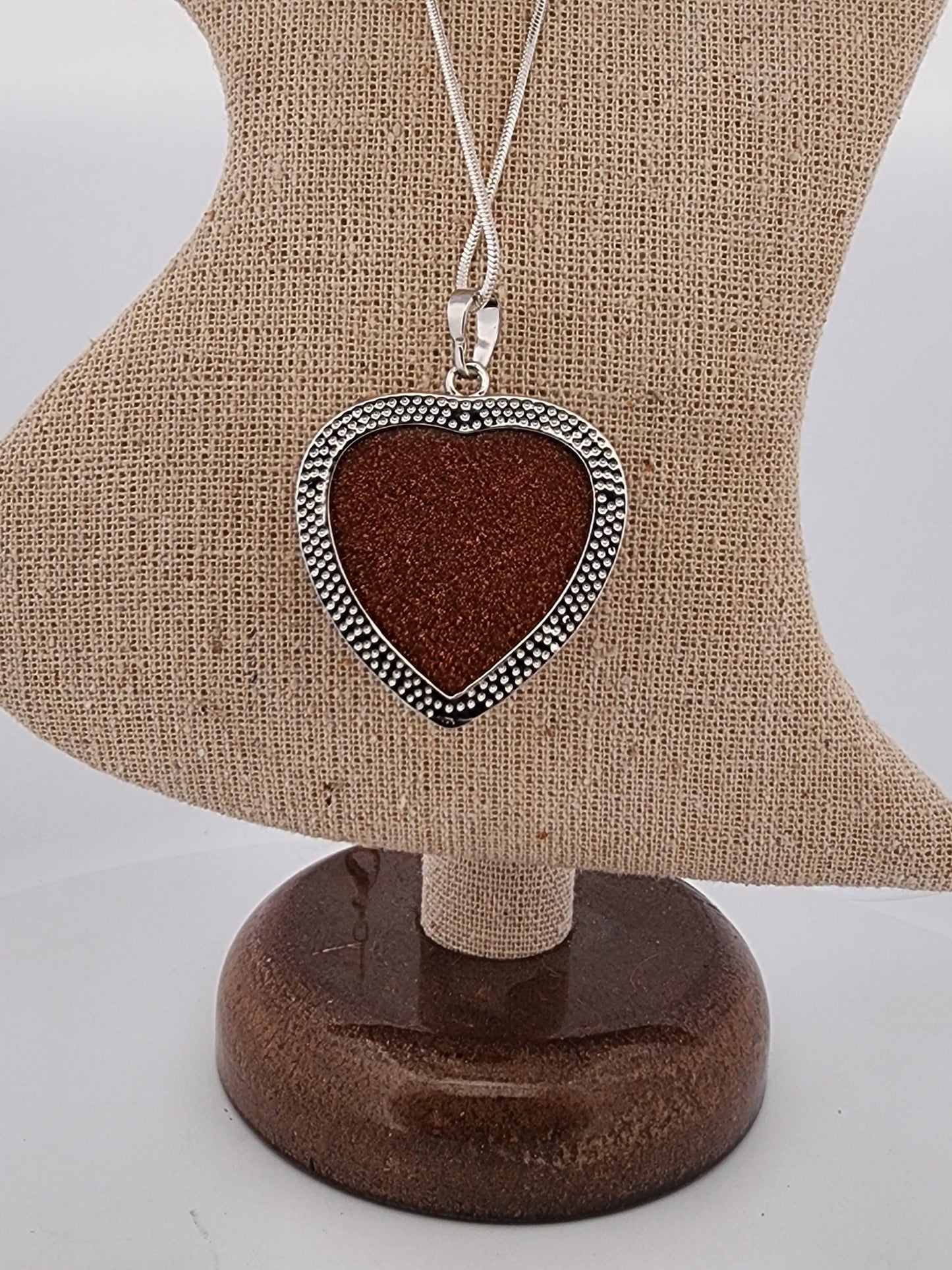 Heart-shaped pendant with brown center and silver border on a mannequin bust.