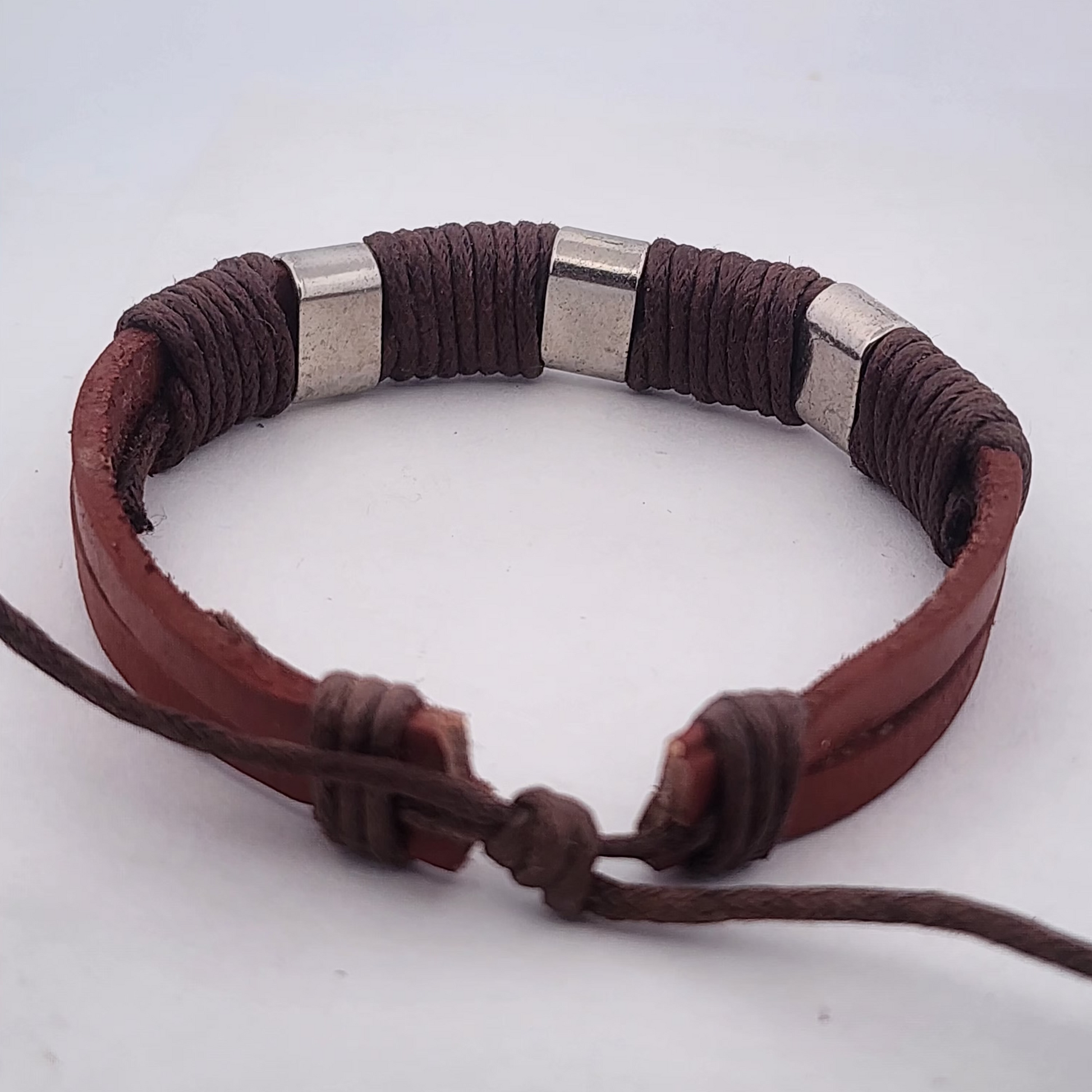 Brown leather bracelet with silver beads on a light gray background