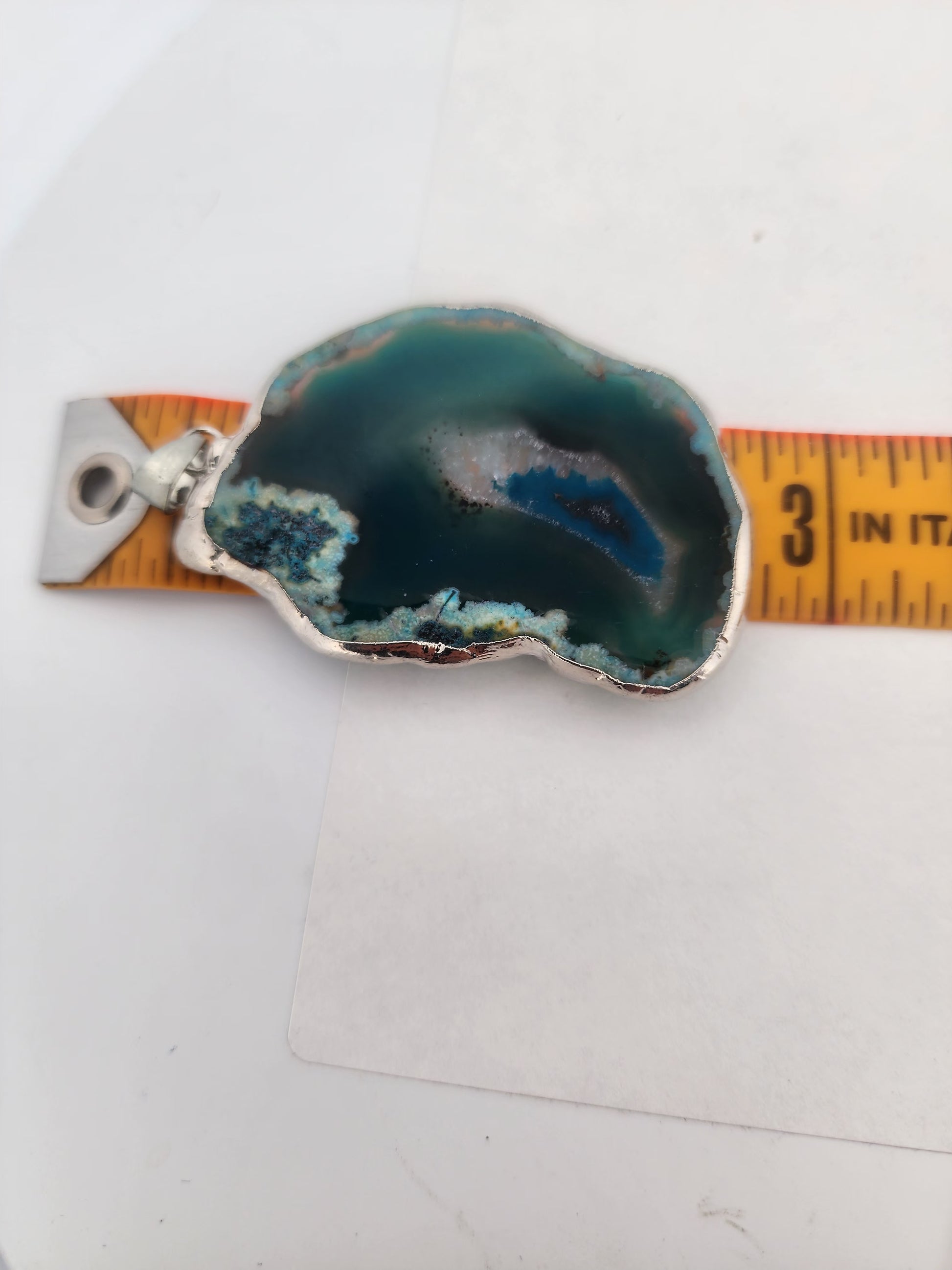 Geode crystal pendant with silver base on a white background, measured by a ruler.