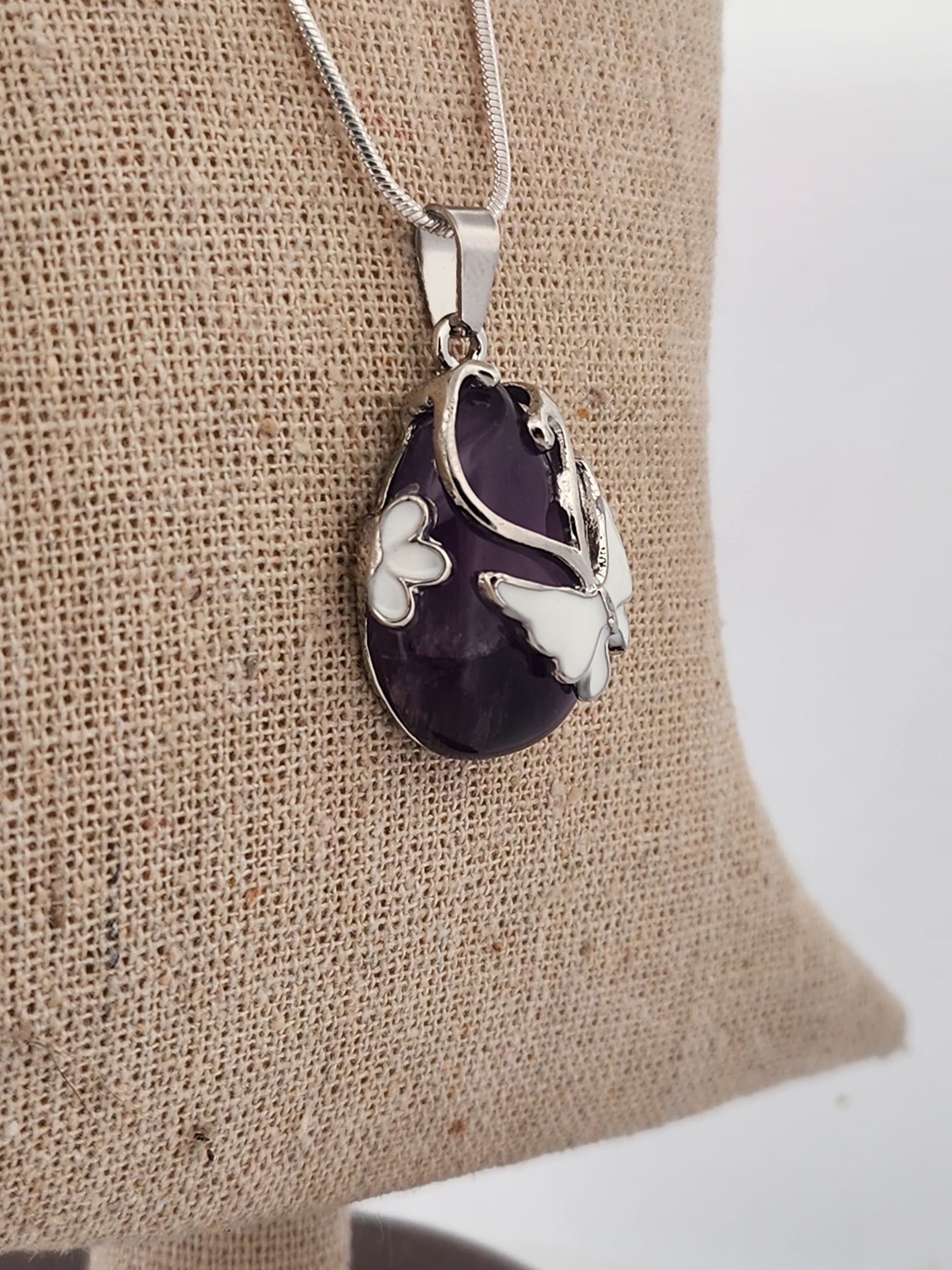 Amethyst pendant with silver butterfly design on a beige fabric background