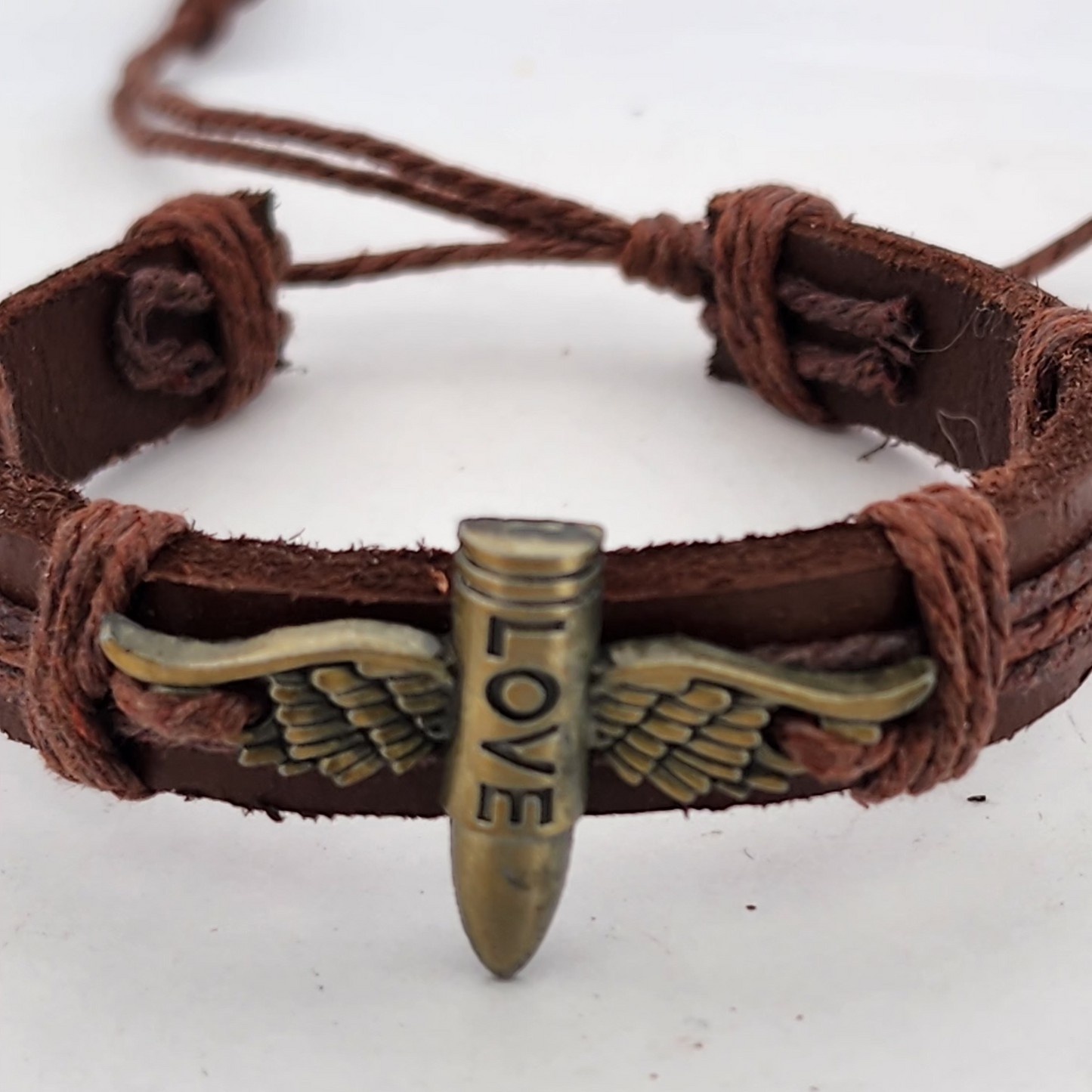 Brown leather bracelet with a bullet-shaped charm featuring wings and the word 'LOVE' on a white background.