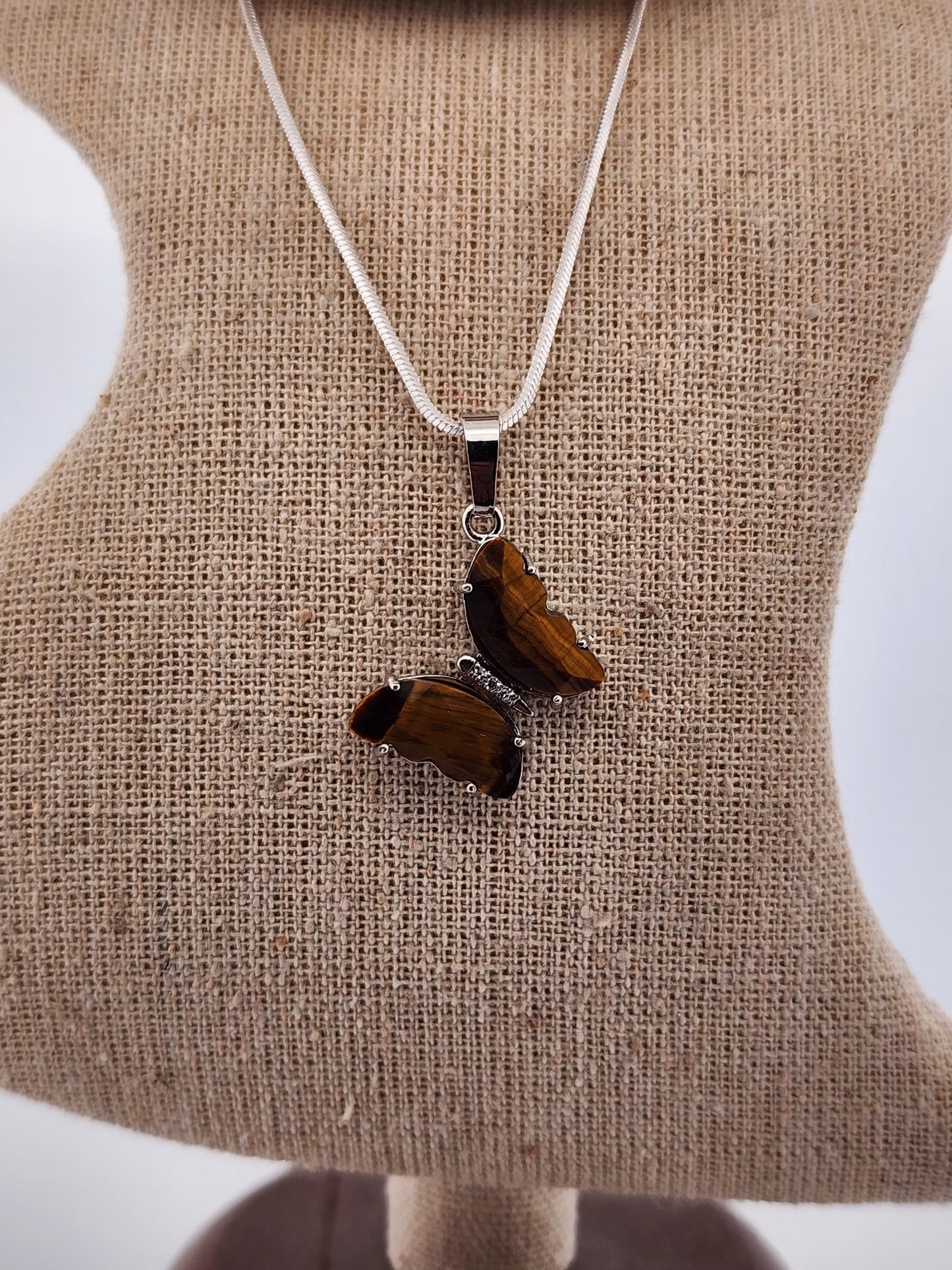 Butterfly-shaped pendant on a necklace against a beige fabric background