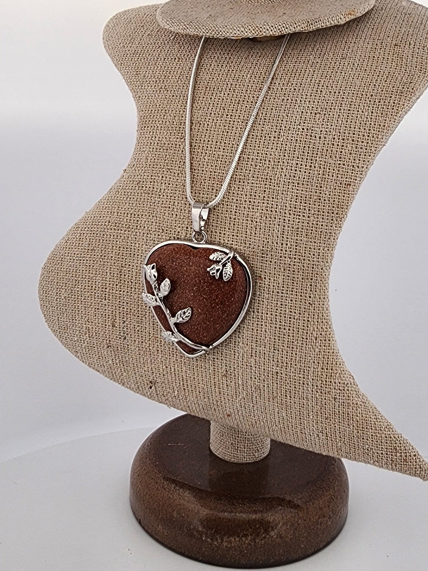 Heart-shaped pendant with leaf design on a necklace, displayed on a heart-shaped mannequin bust.