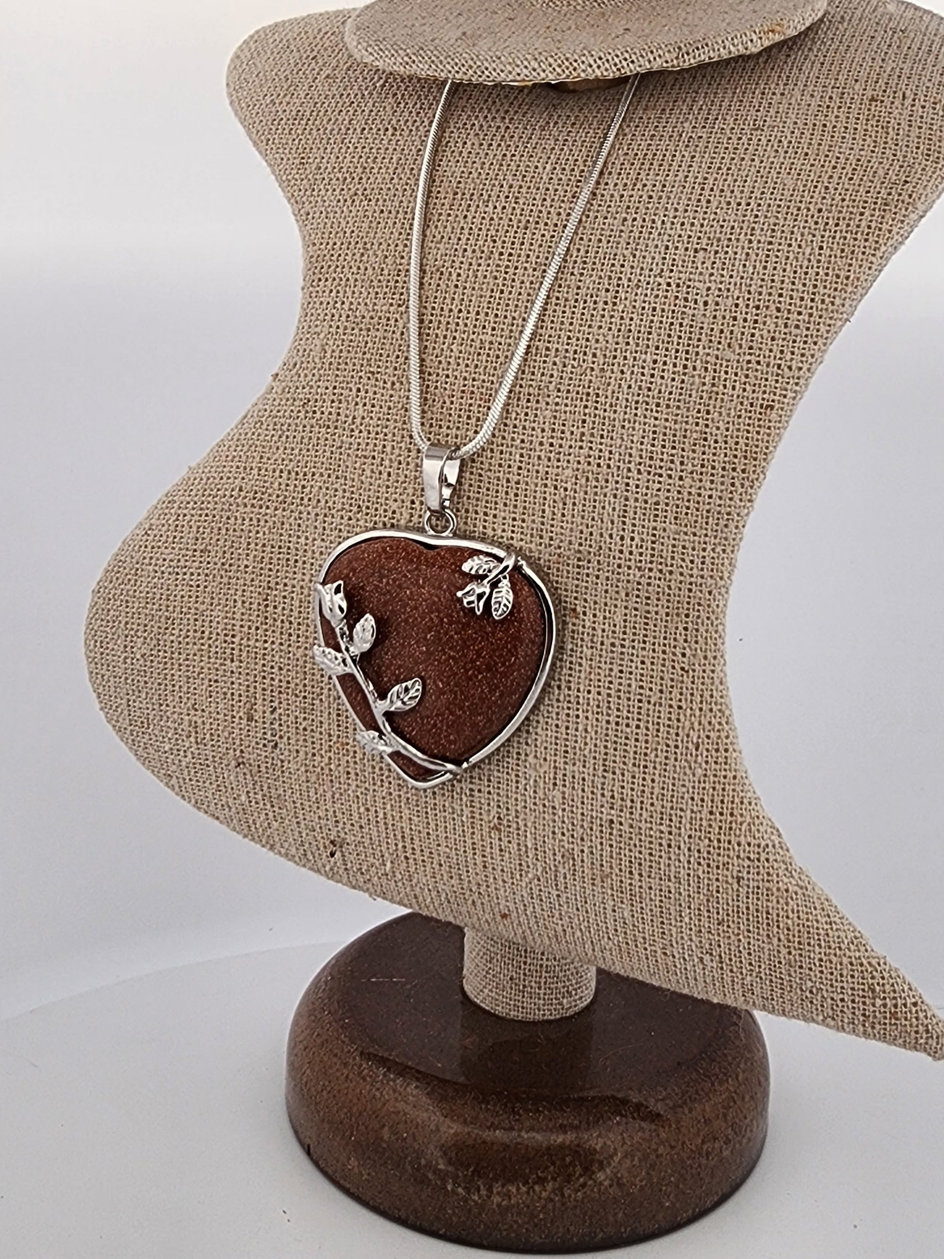 Heart-shaped pendant with leaf design on a necklace, displayed on a heart-shaped mannequin bust.