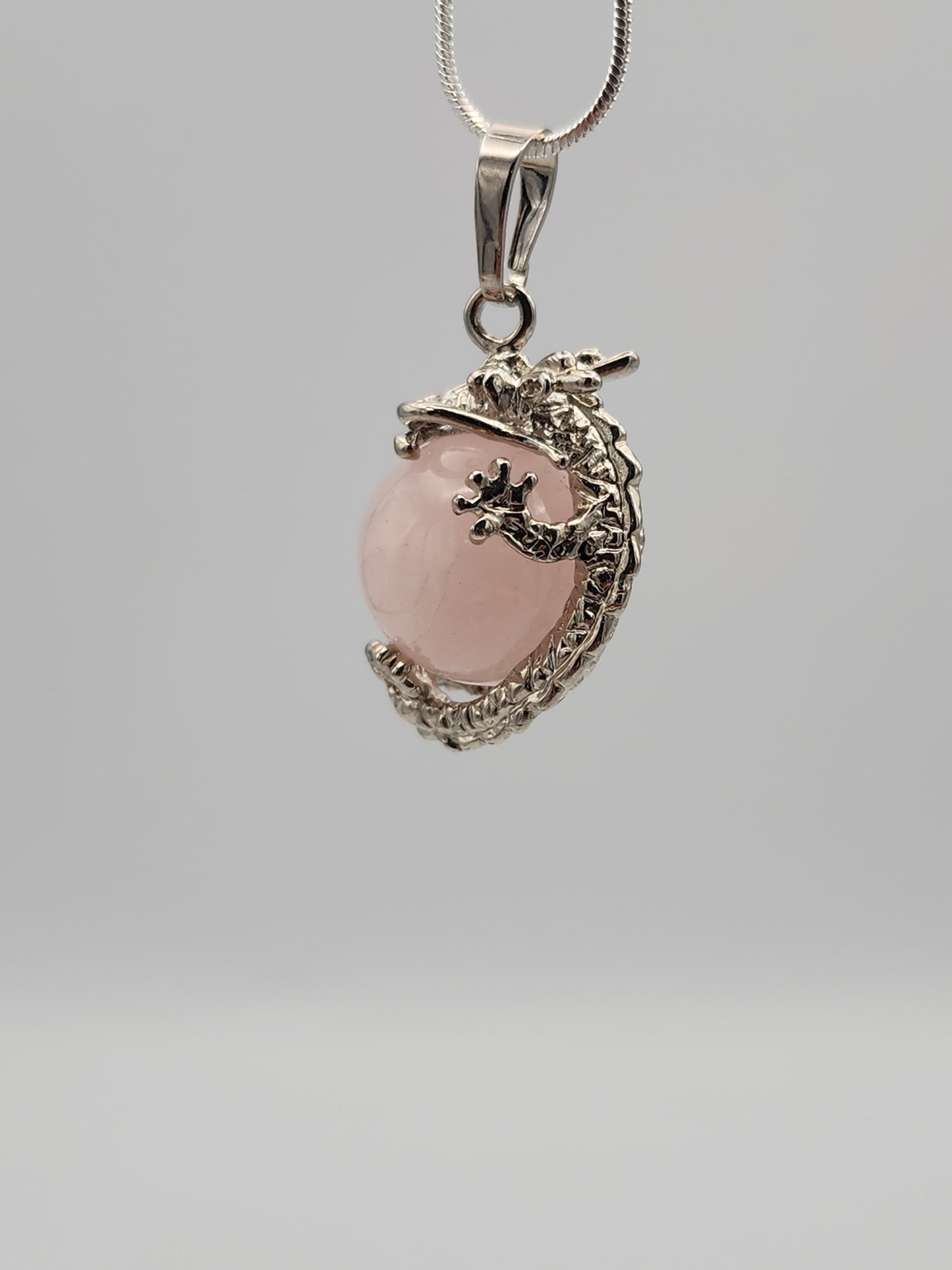 Pink stone pendant with silver dragon design on a gray background