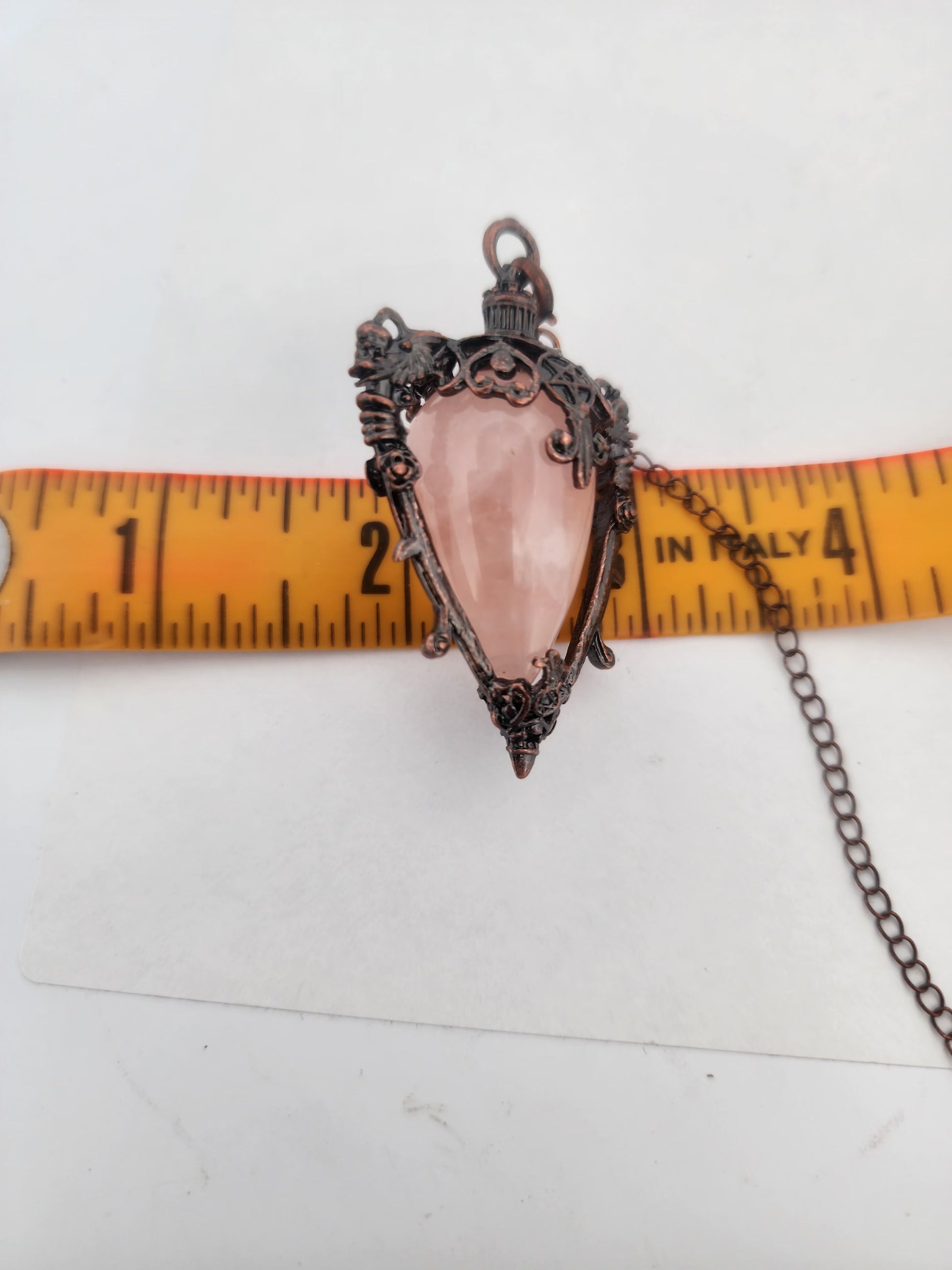 Pink crystal pendant with chain on a white background with a ruler for scale.