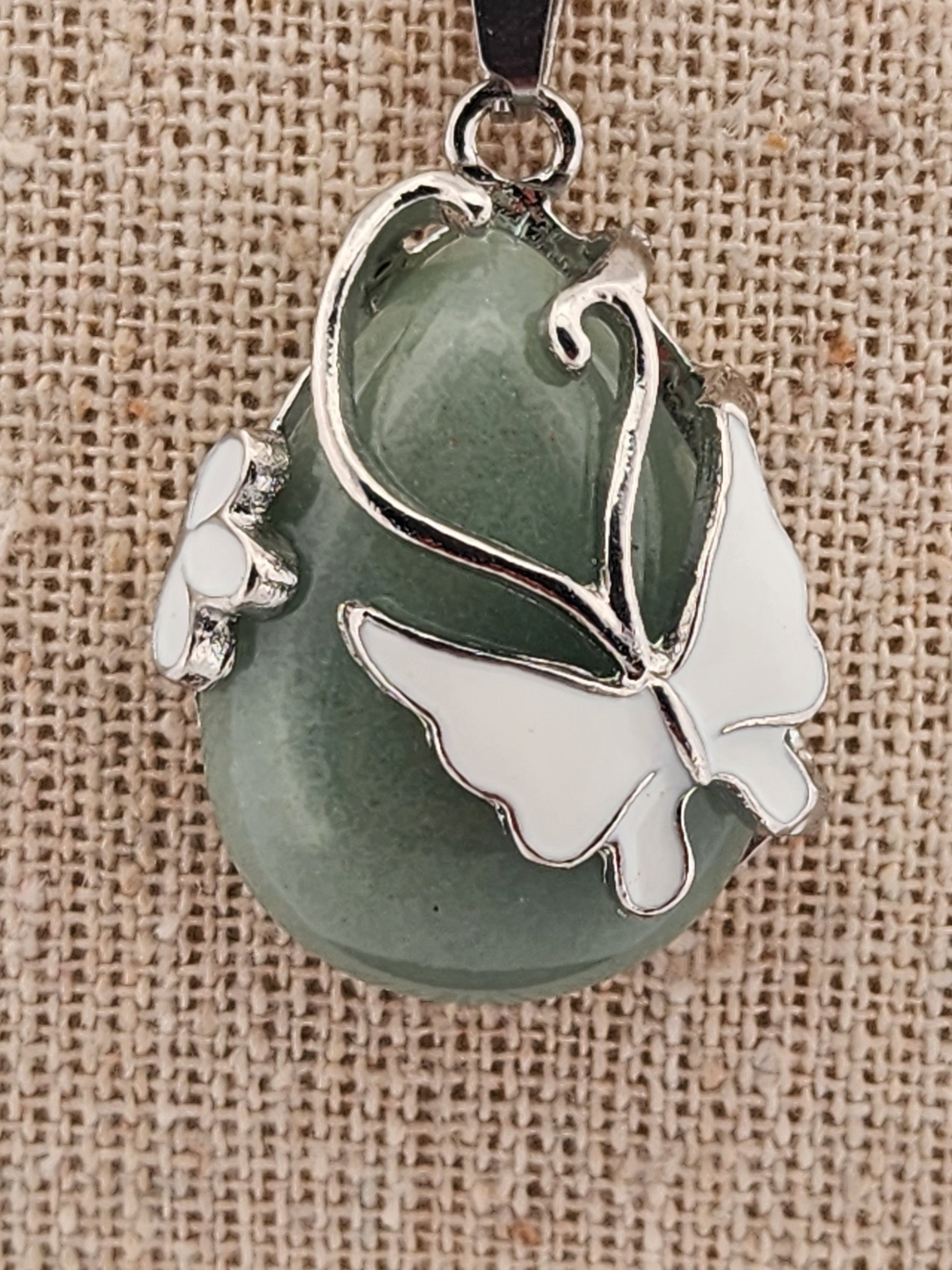 Green stone pendant with silver butterfly design on a textured beige background