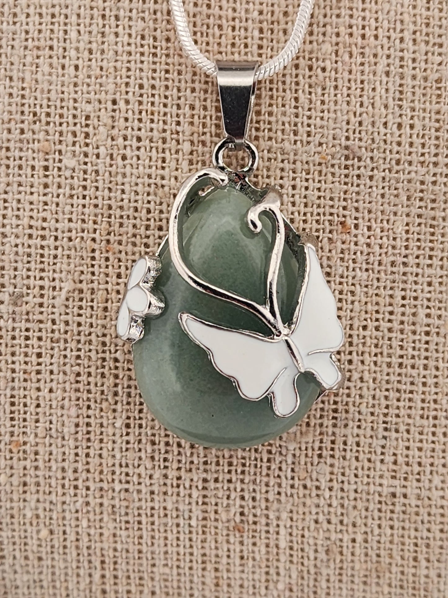 Green stone pendant with silver butterfly design on a beige fabric background