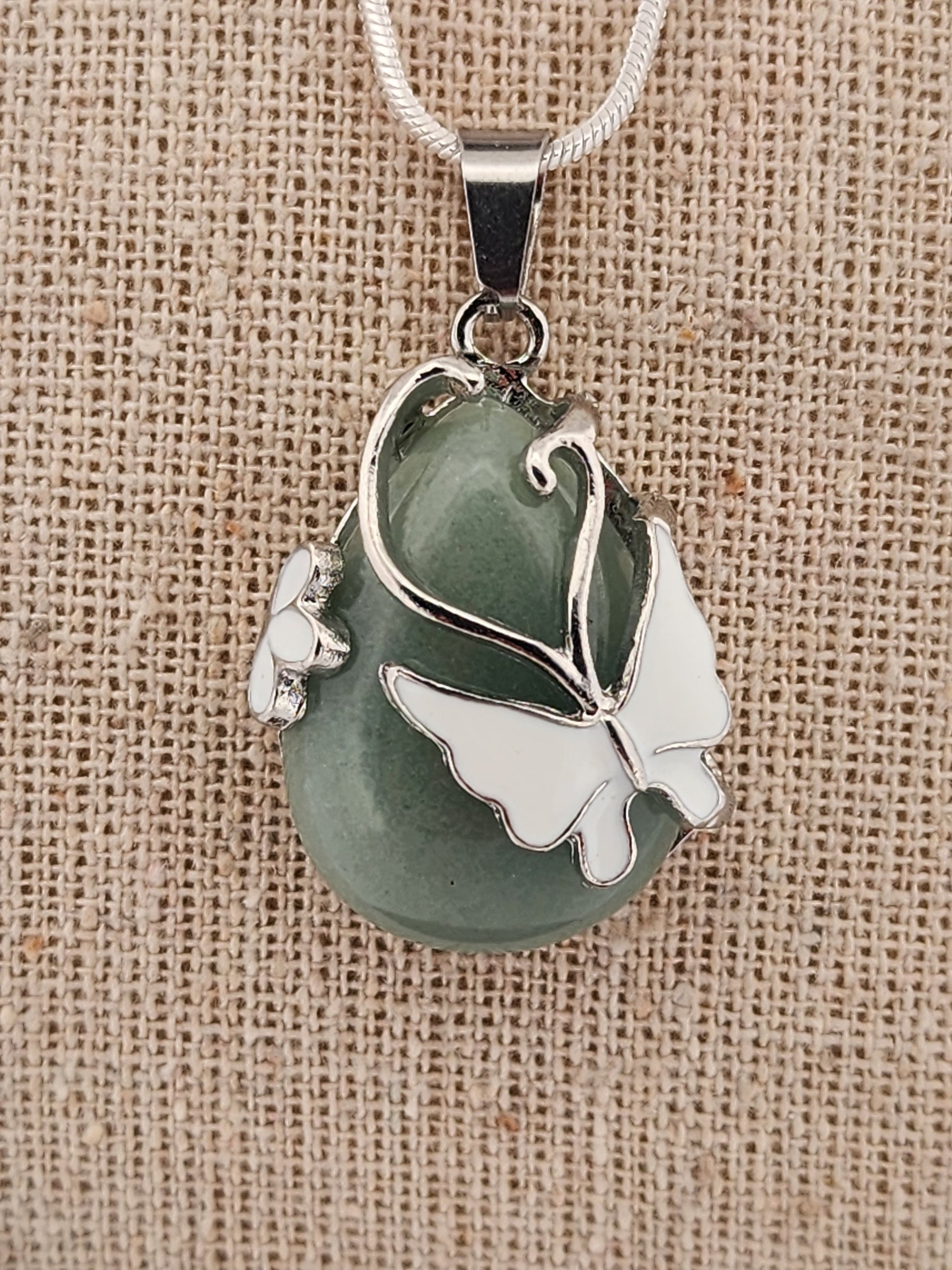 Green stone pendant with silver butterfly design on a beige fabric background