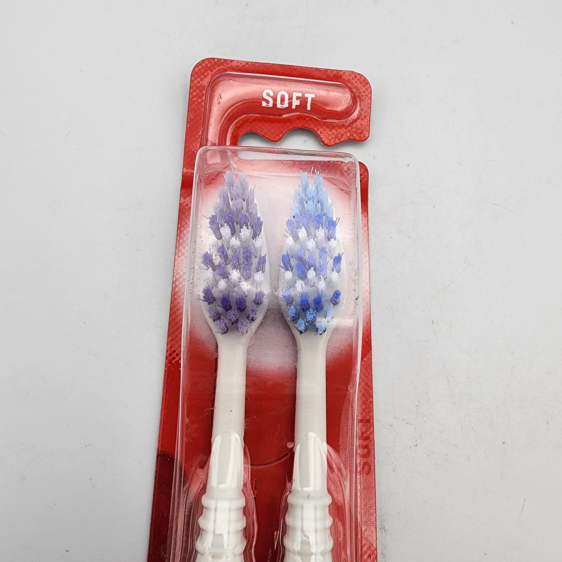 Two toothbrushes with blue bristles in a red packaging on a gray background