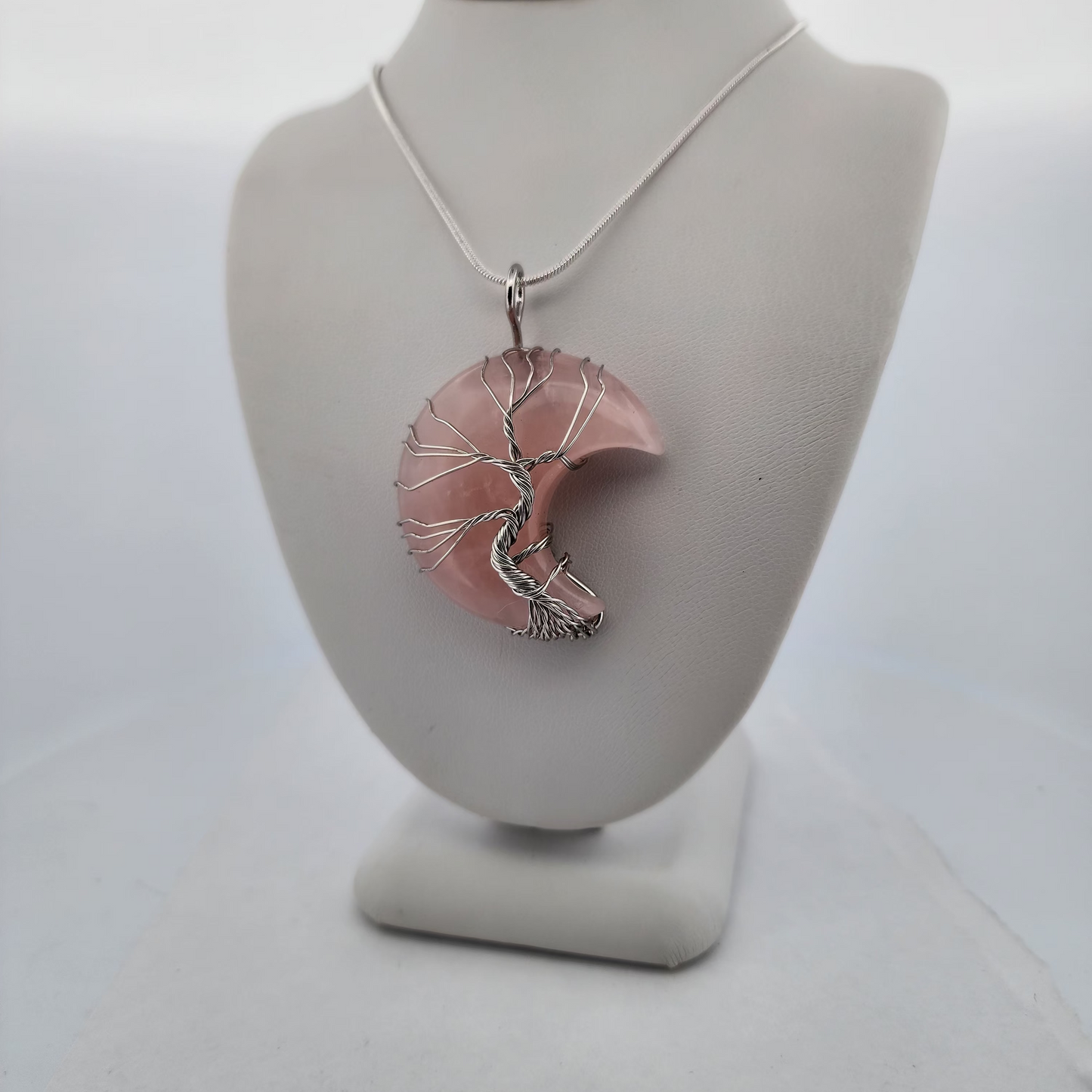 Necklace with a pink and silver pendant on a gray mannequin bust against a white background