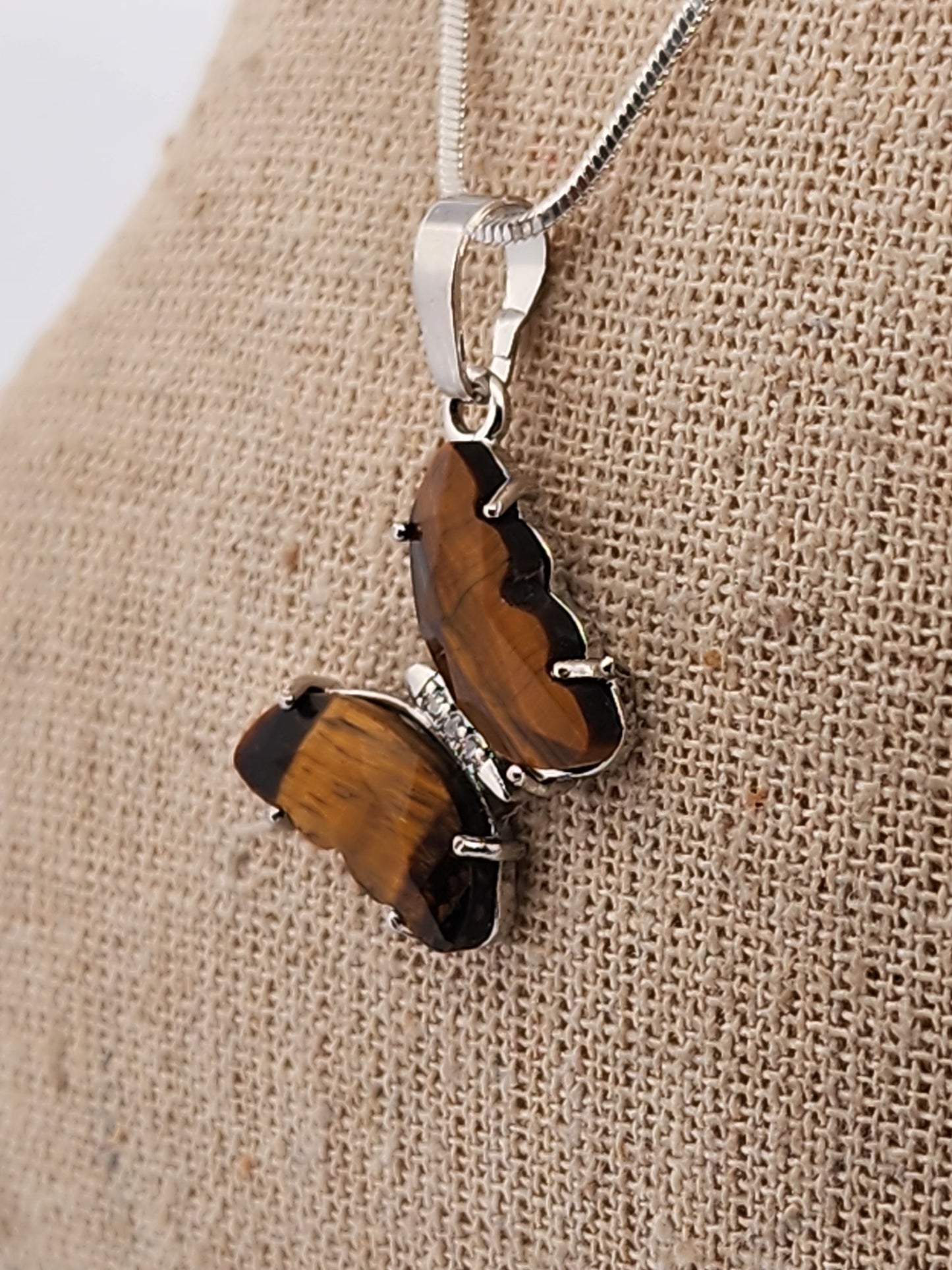Butterfly-shaped pendant with brown wings and silver body on a beige fabric background