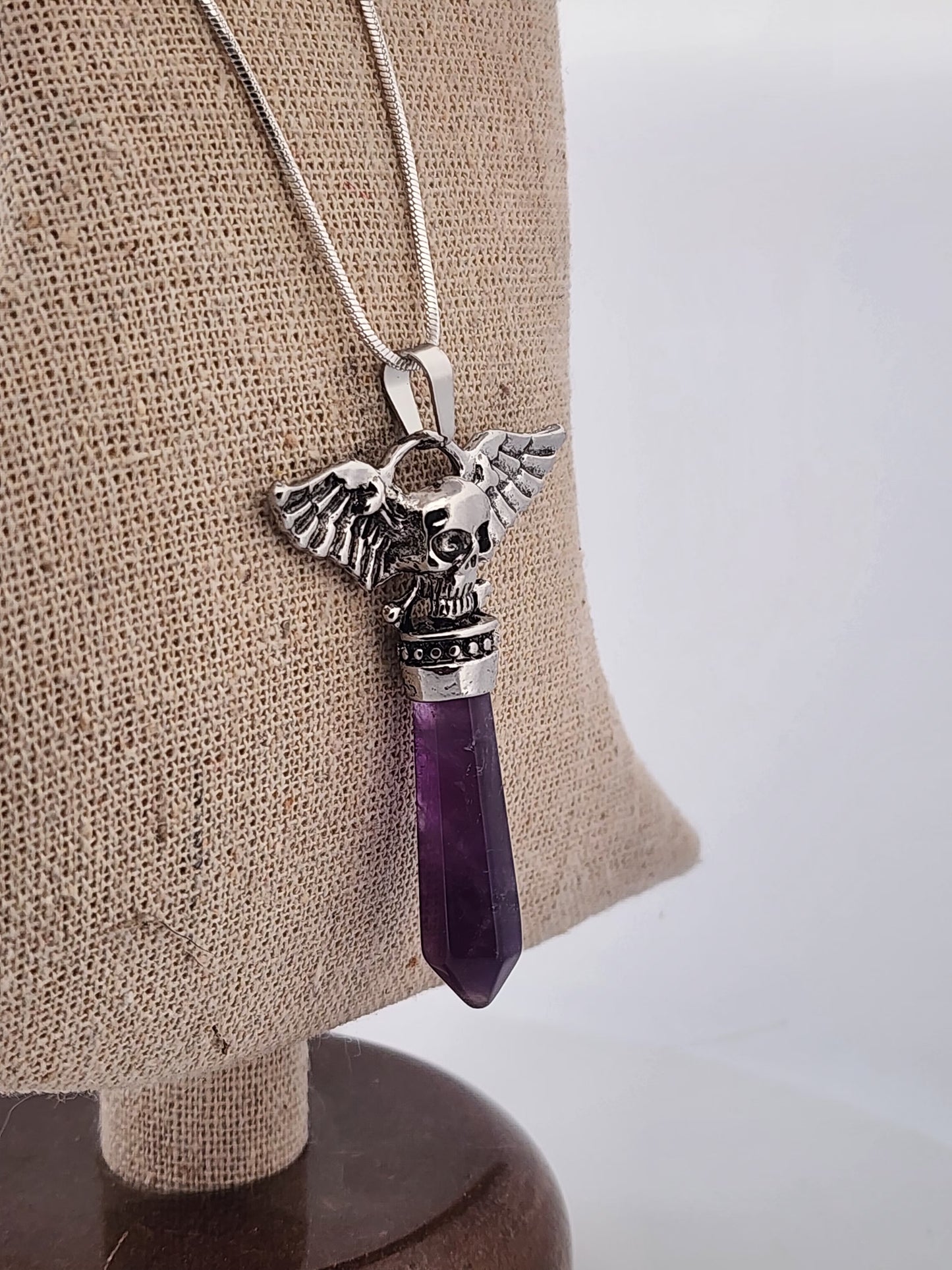 Amethyst pendant with silver angel wing design on a mannequin bust.