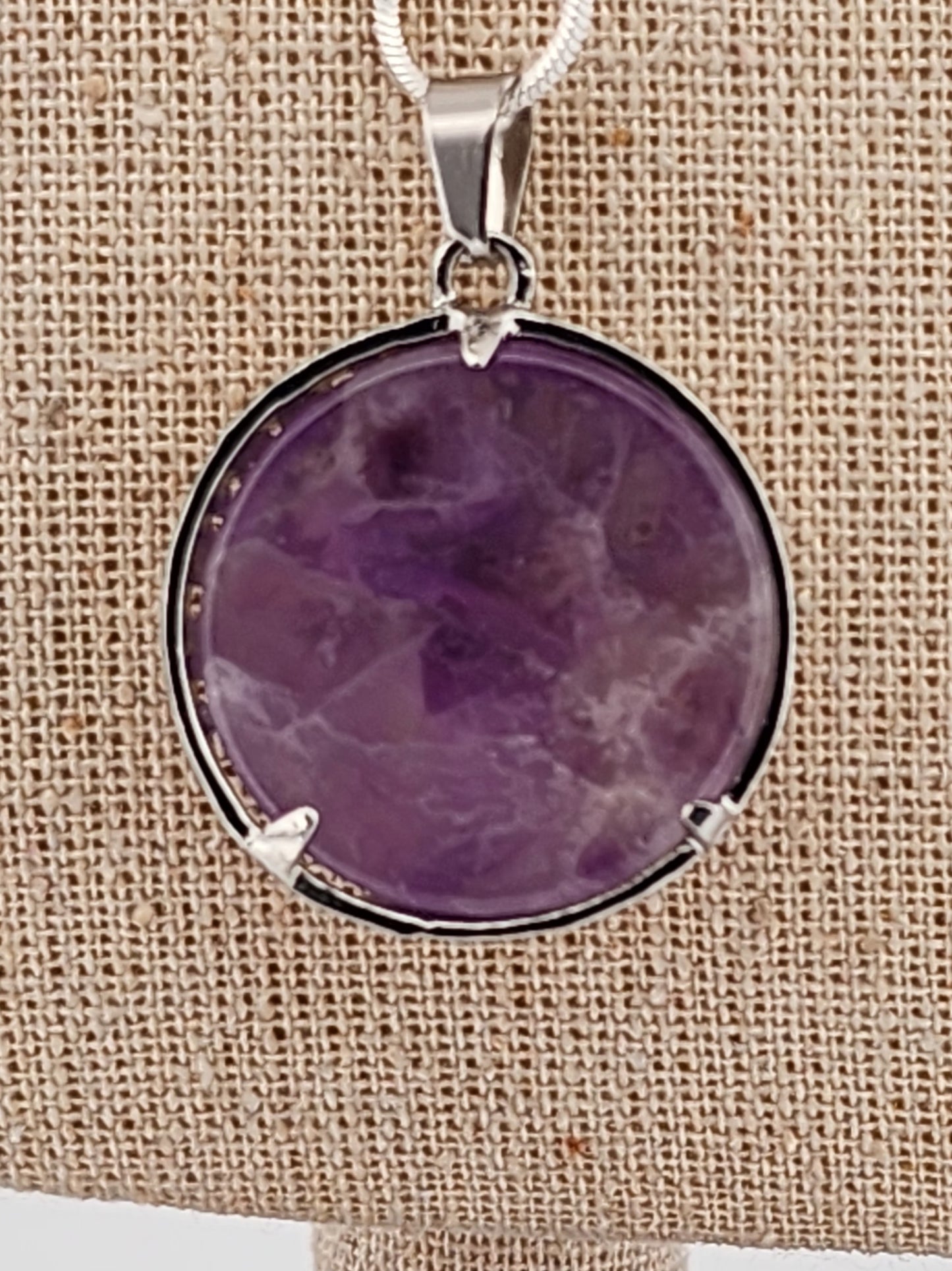 Purple stone pendant on a beige fabric background